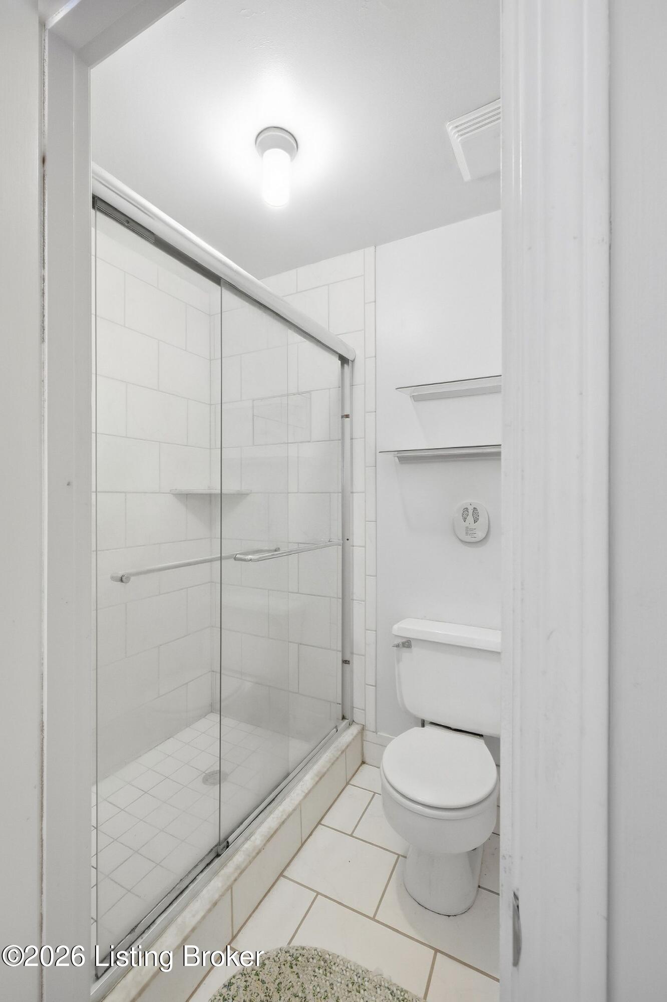 Bathroom with a glass-enclosed tiled shower, corner shelf, toilet, and wall-mounted shelves.