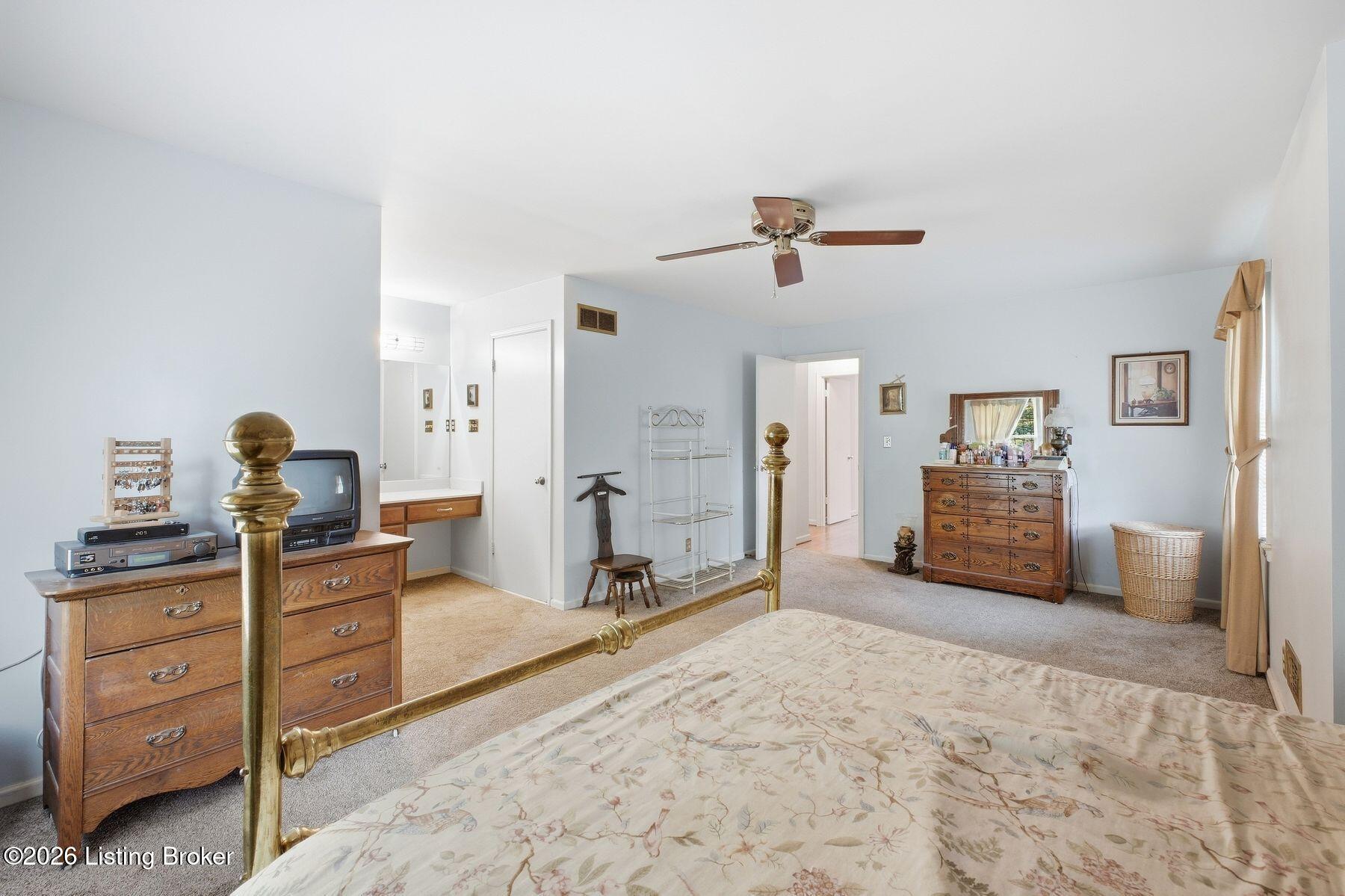 Furnished bedroom with a brass bed, floral bedspread, wooden dressers, and pale blue walls.