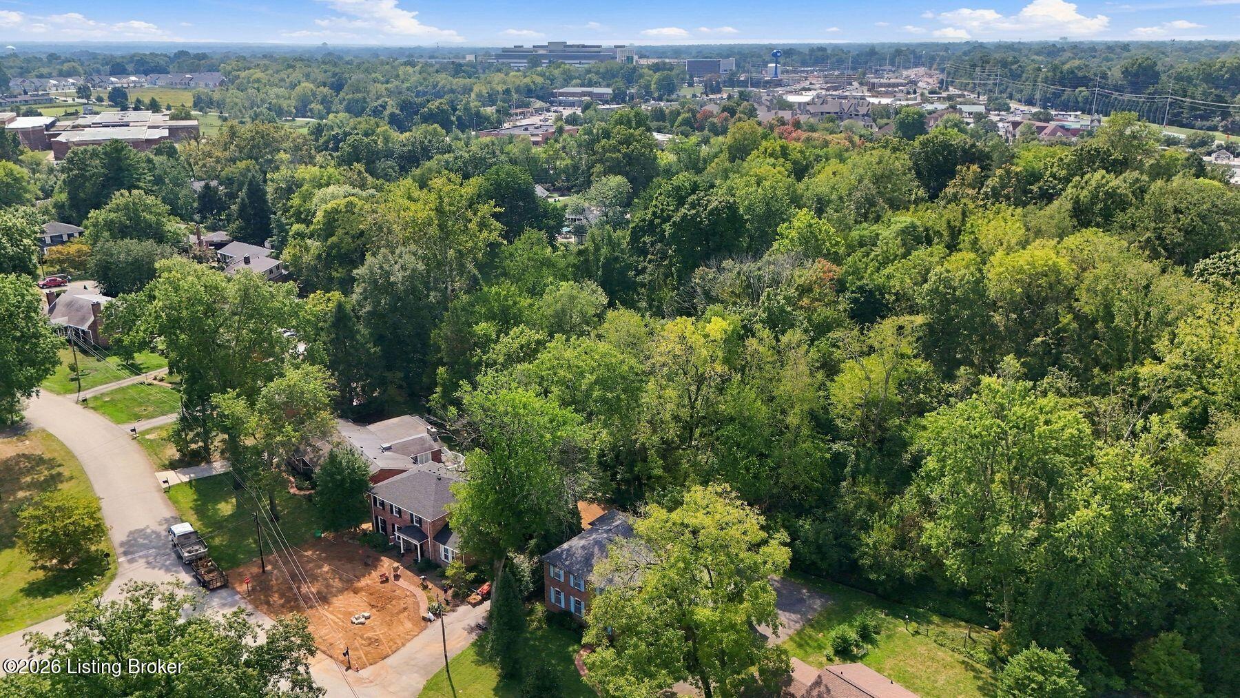 Aerial view of a tree-covered neighborhood with a construction site in the foreground.
