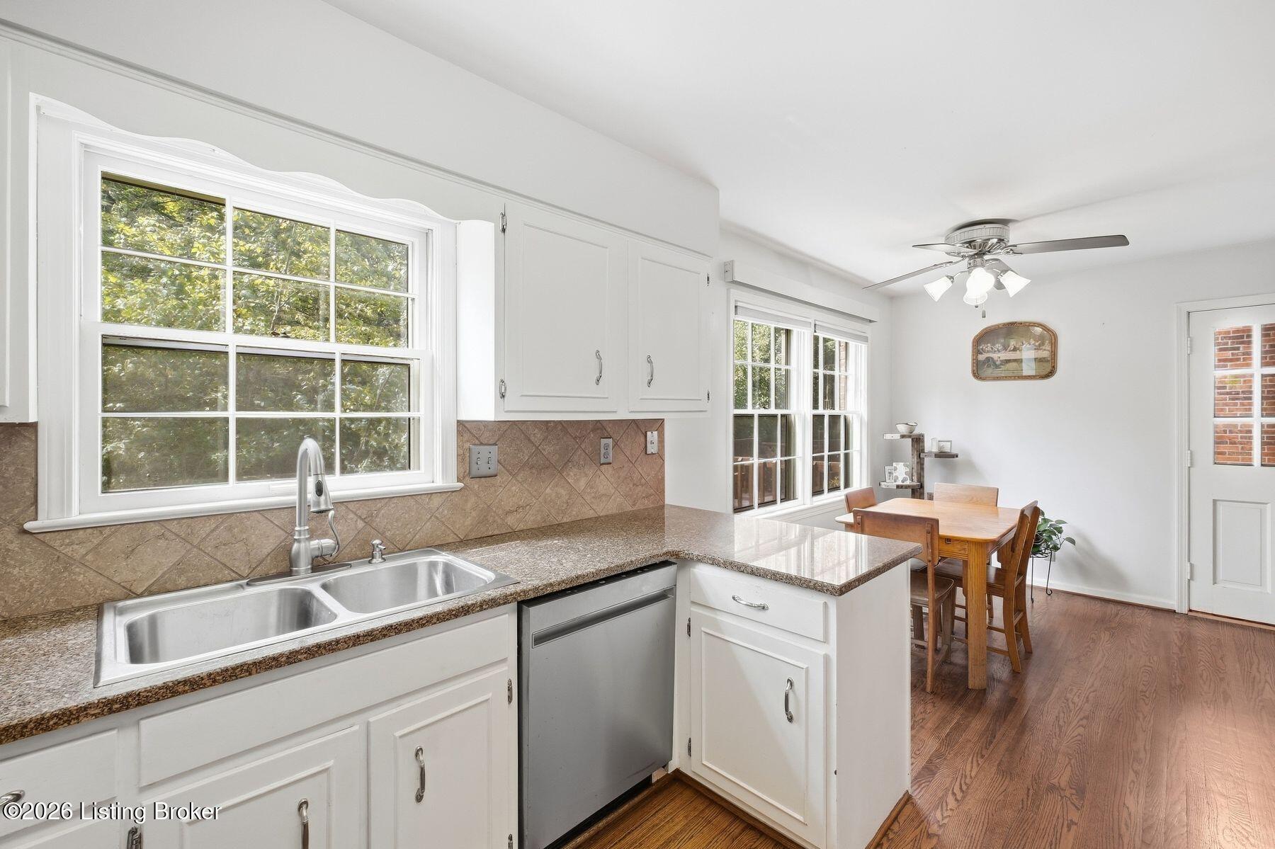 Bright kitchen with white cabinets, granite counters, double sink, and adjoining dining area with hardwood floors.