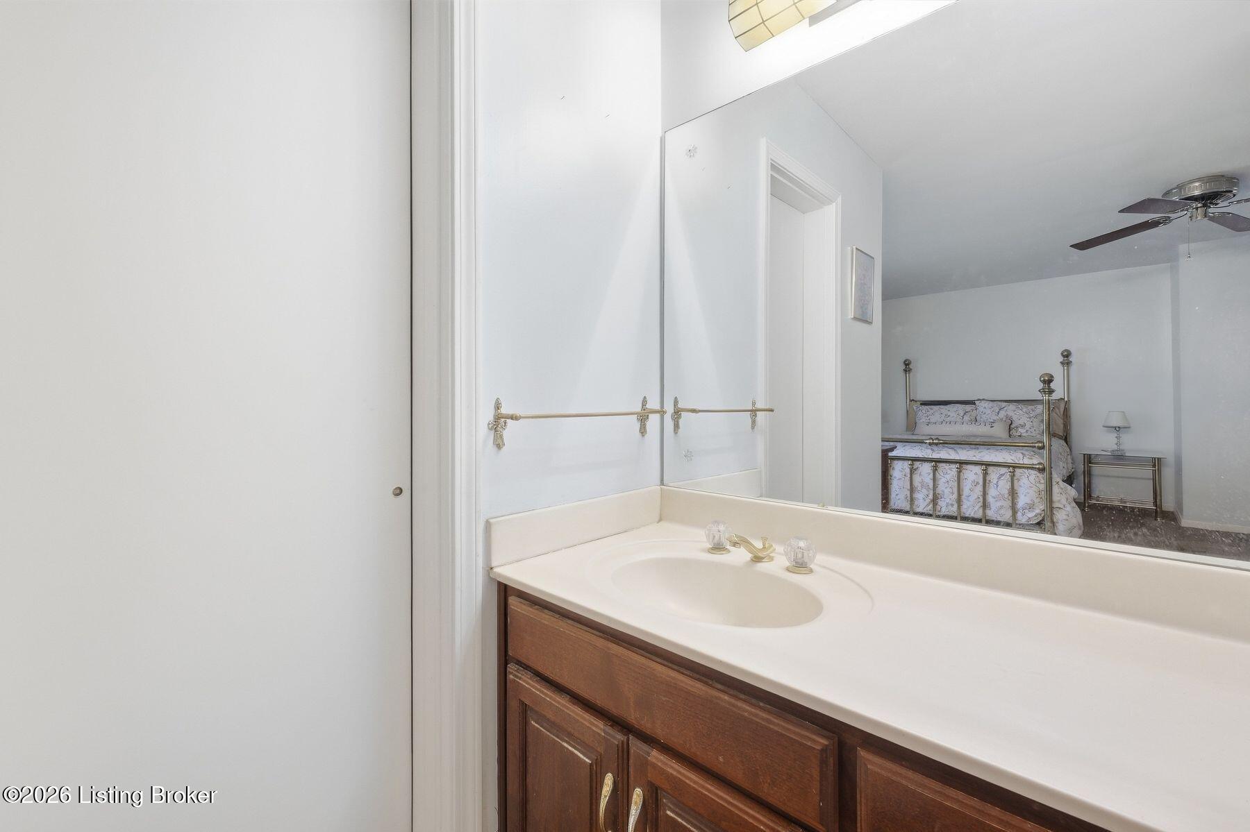 Bathroom vanity and mirror reflecting a bedroom with a brass bed.