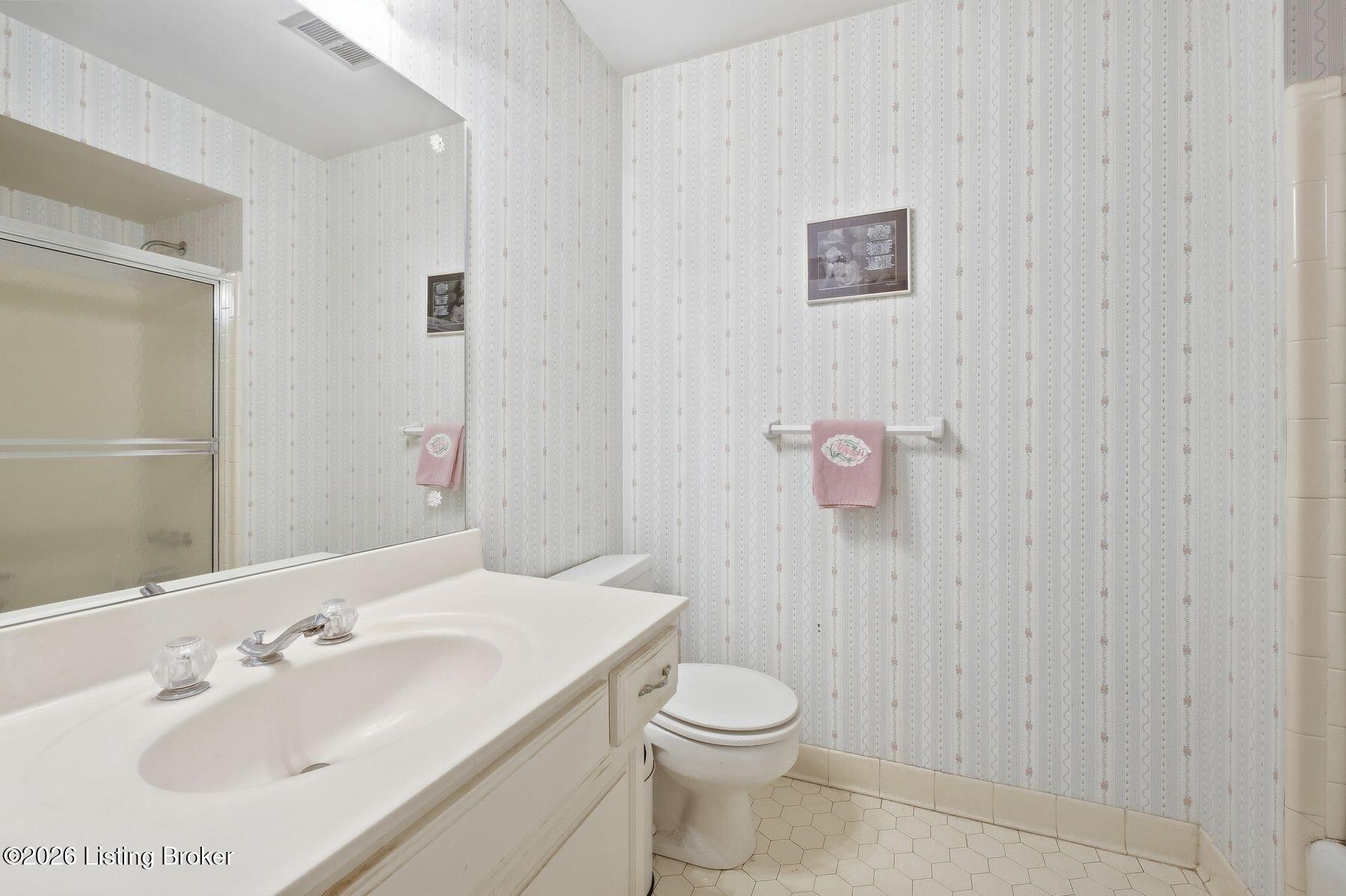 Bathroom with a large white vanity, toilet, patterned wallpaper, and pink towels.