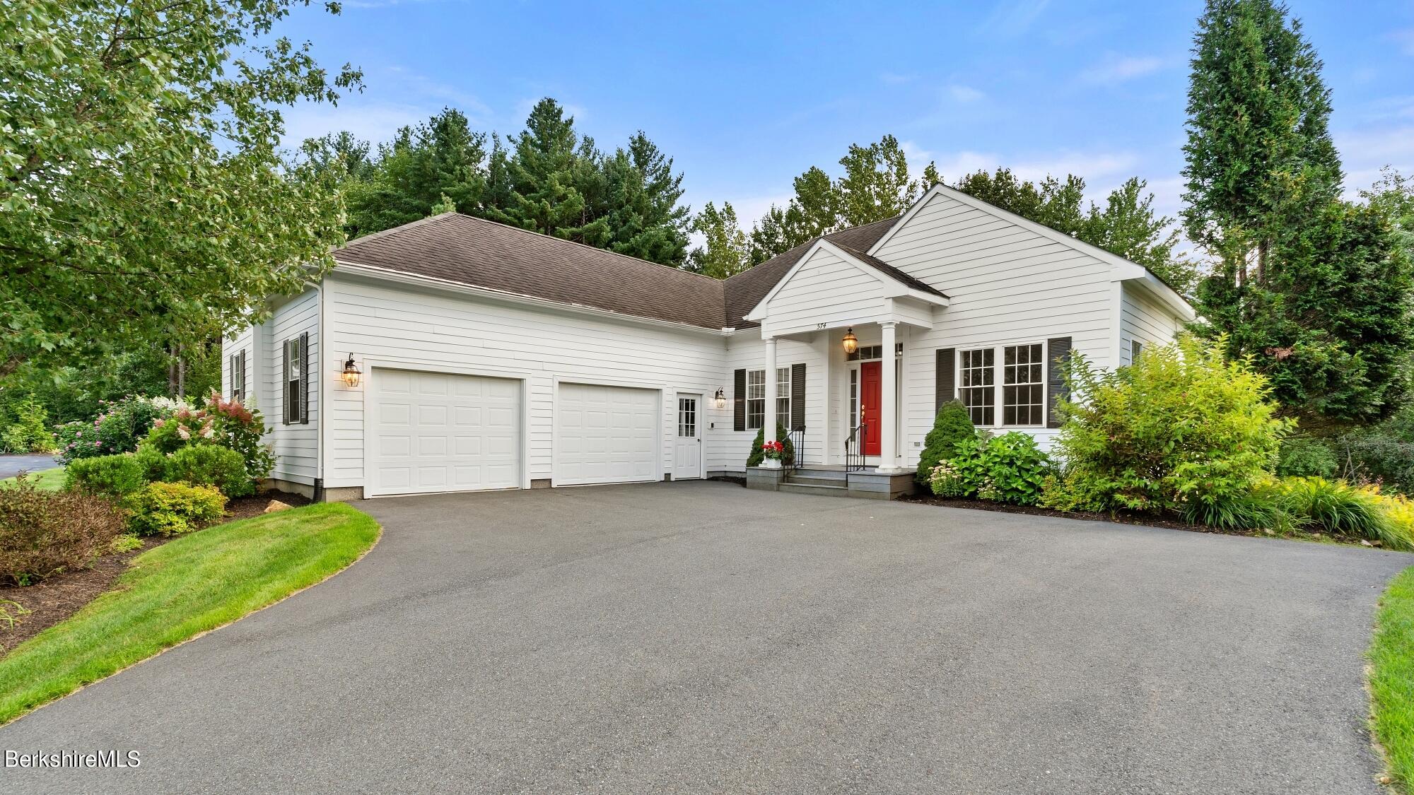 White-sided house with a two-car garage, red front door, covered porch, and landscaped gardens.