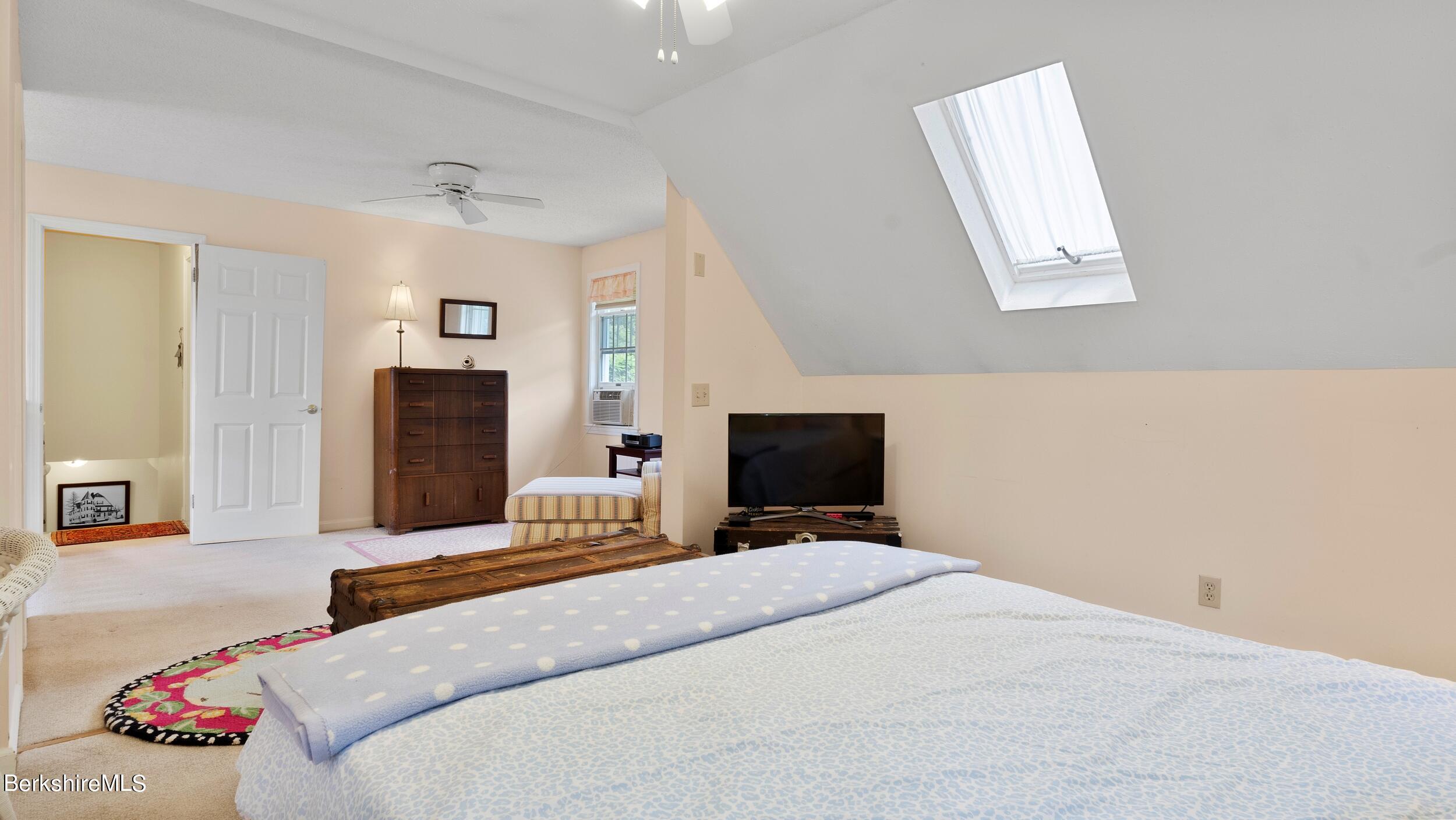 Furnished bedroom with a skylight set into its sloped ceiling and a large bed.