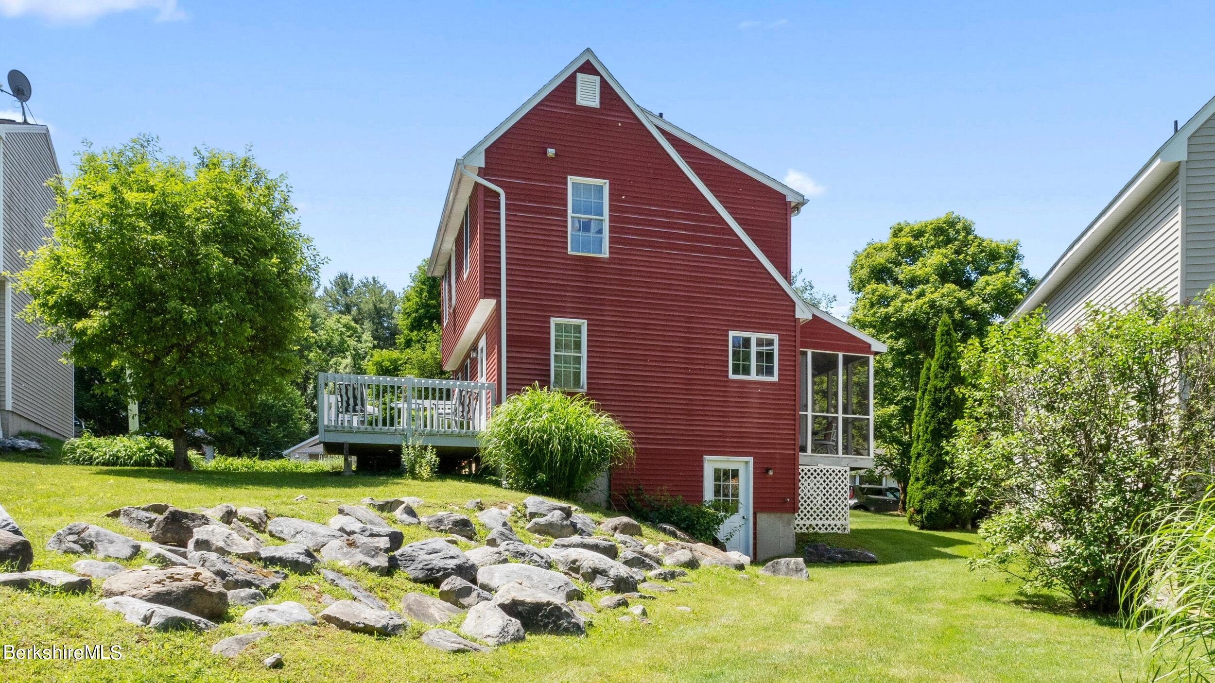 Red-sided house with a white-railed deck, screened porch, and rock-bordered lawn.