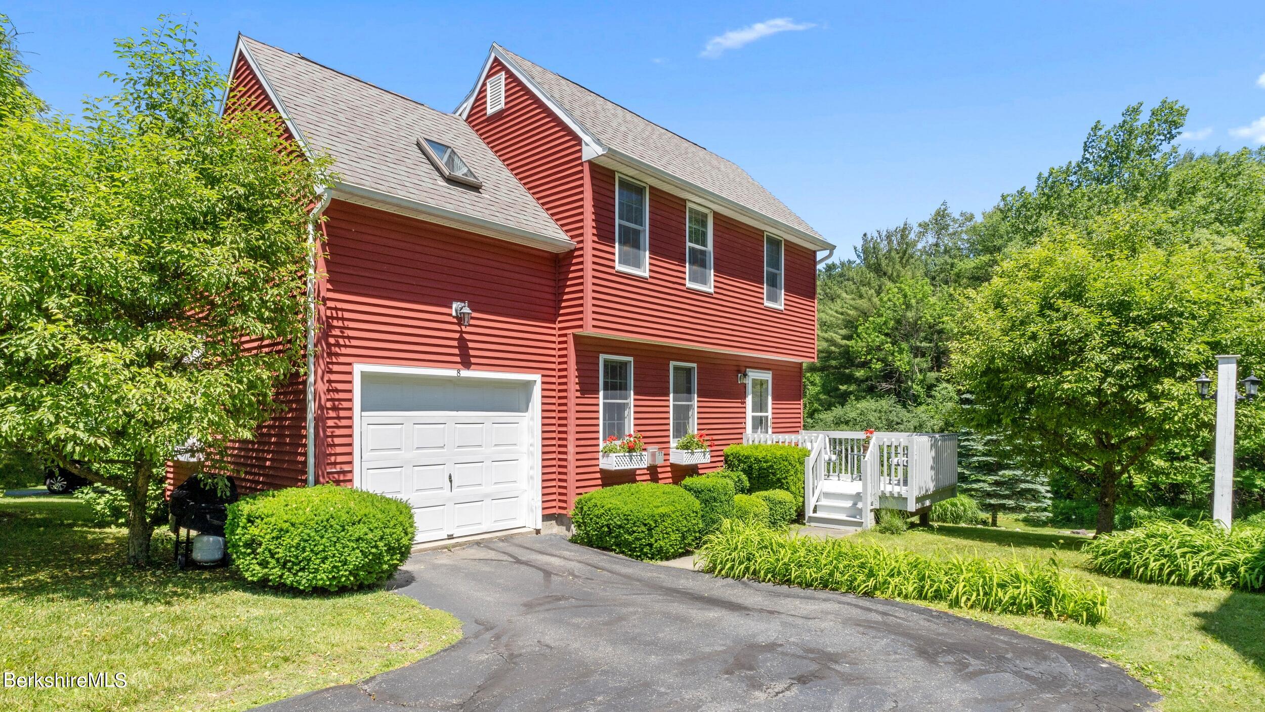 Red two-story house with an attached garage, white deck, and landscaped yard.