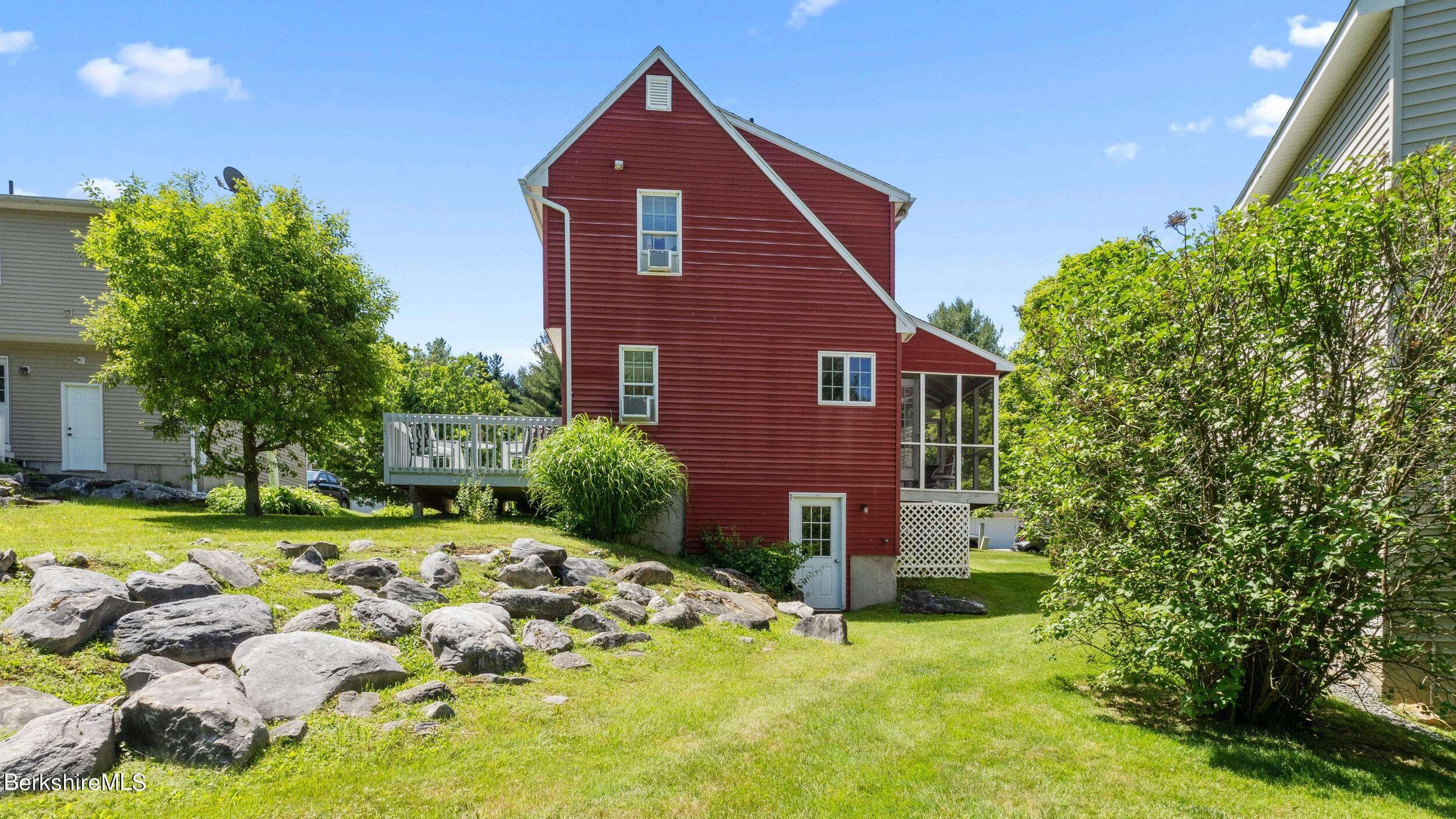 Red-sided house with a raised deck, screened porch, and rock-lined lawn.