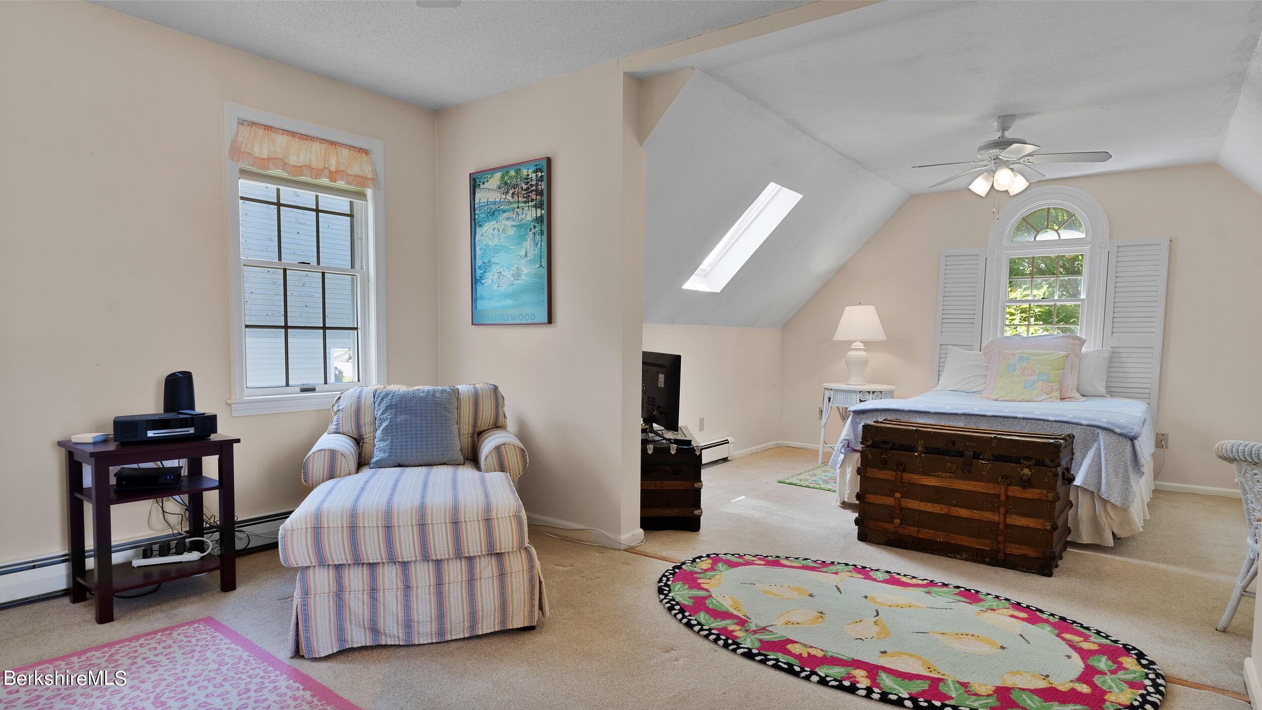 Upper-level bedroom with skylight, arched shuttered window, wooden trunk, and striped sitting chair.