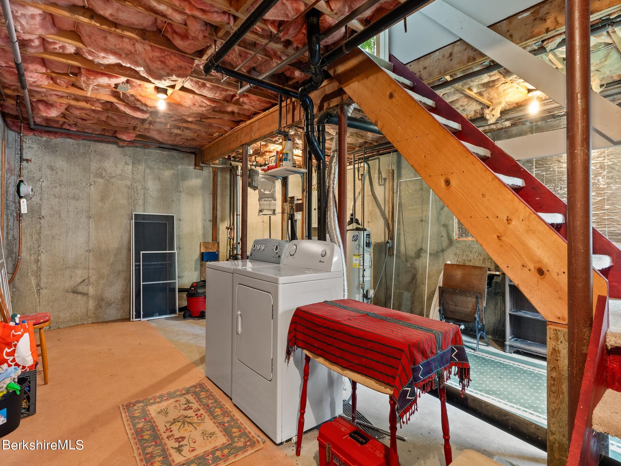 Basement laundry area with washer and dryer beneath an open wooden staircase.