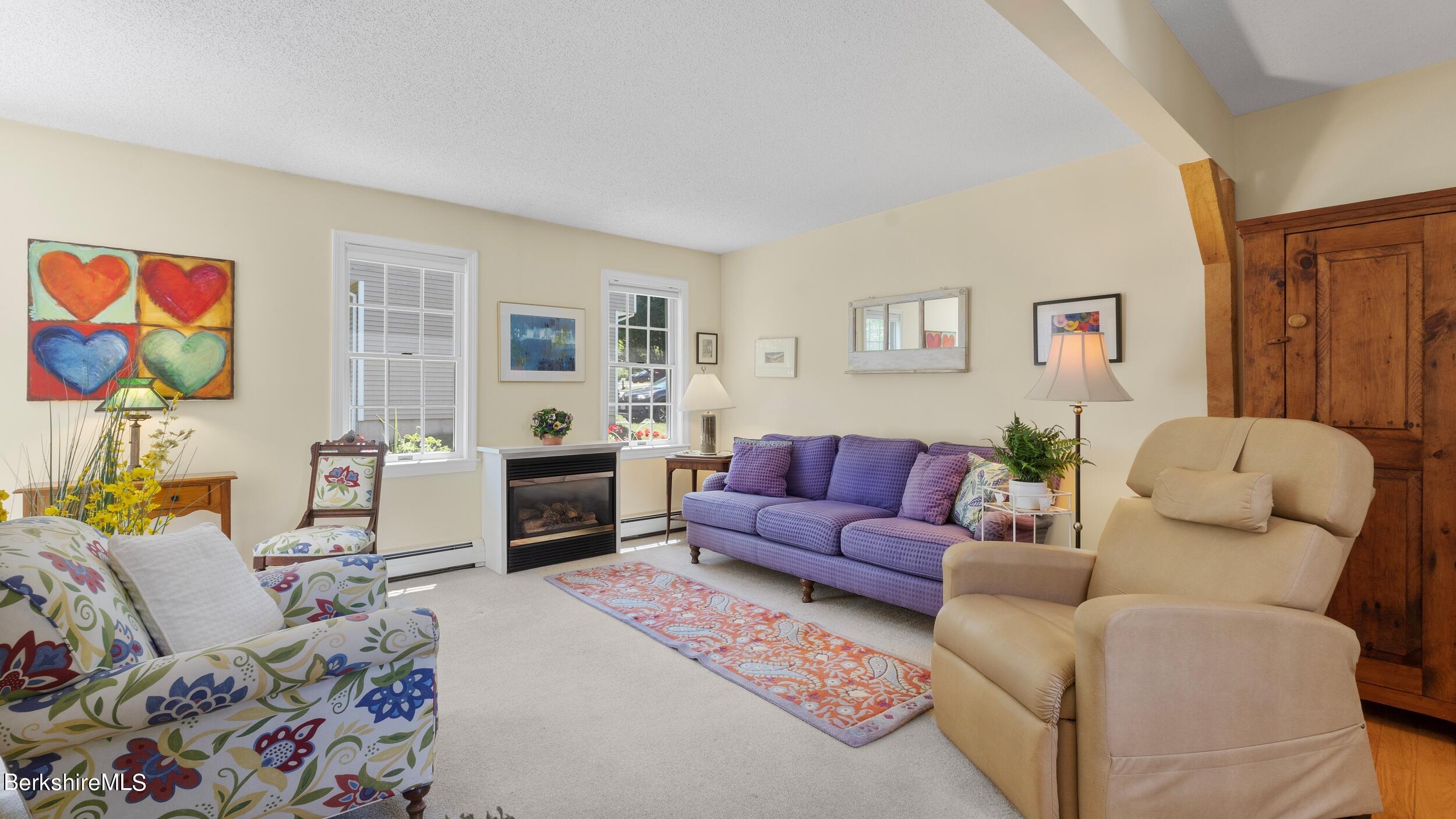 Living room with a purple sofa, patterned armchairs, gas fireplace, and large wooden cabinet.