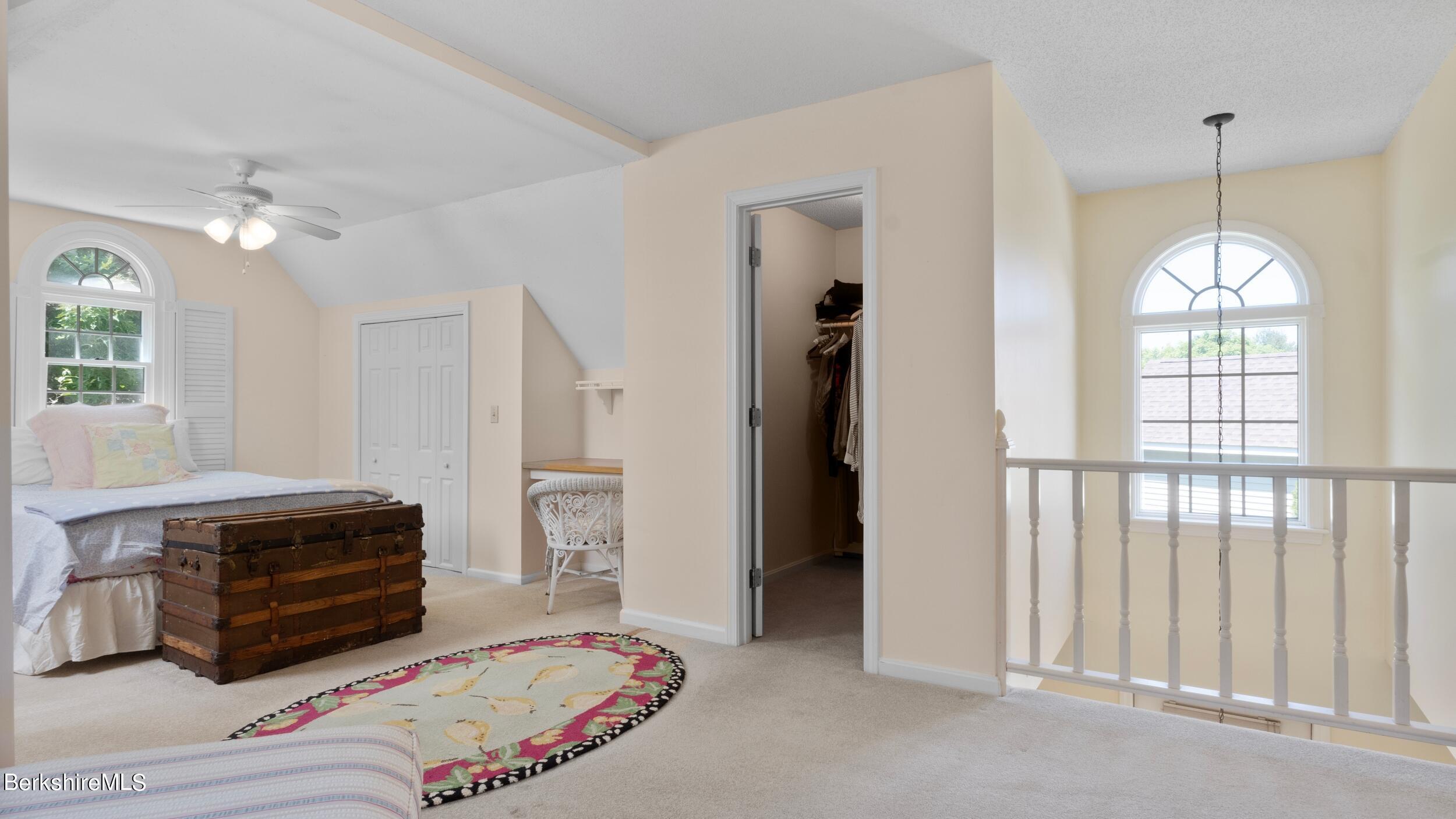 Upstairs bedroom with a wooden trunk, colorful rug, and arched windows overlooking the landing.