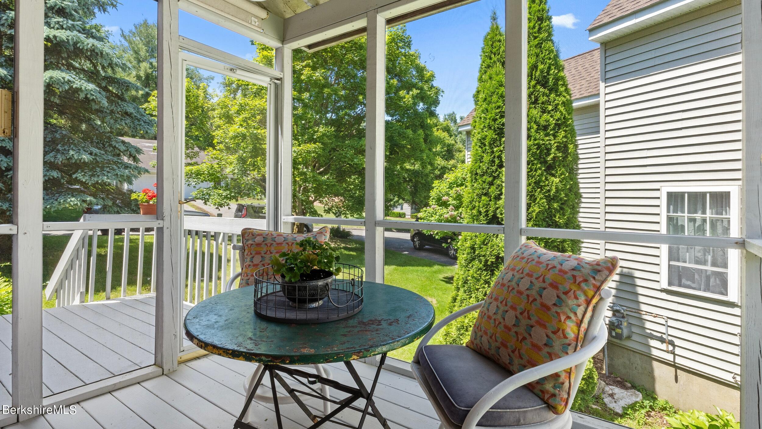 Screened porch with a round table and cushioned chair overlooking trees and a green lawn.