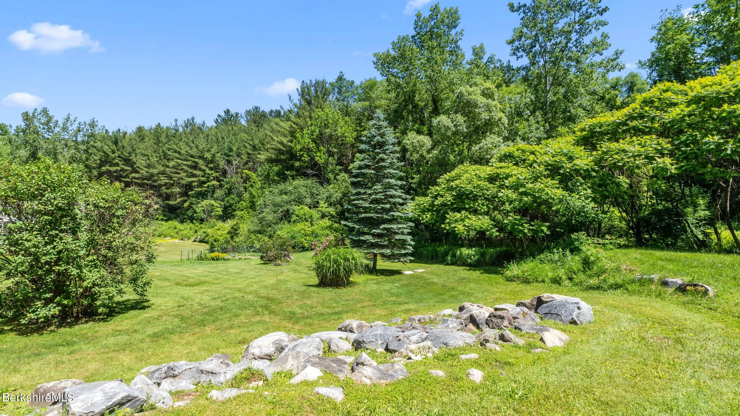 Landscaped lawn with a curved stone border and a dense wooded backdrop.