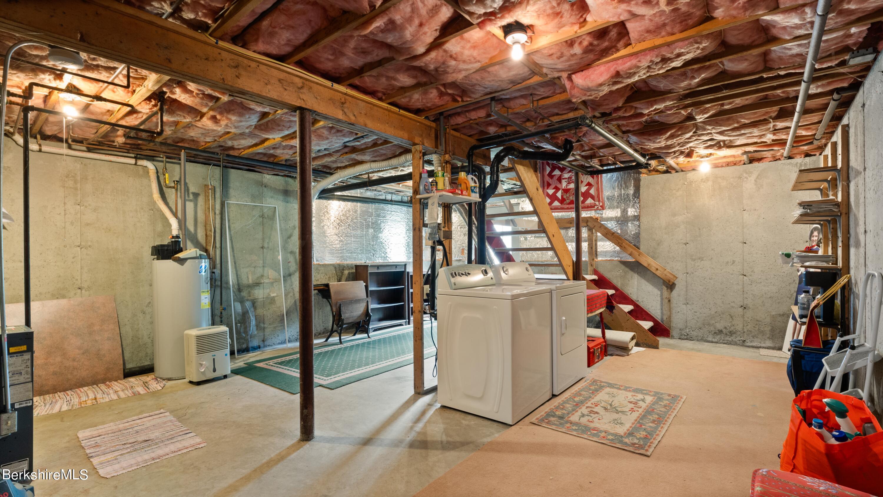 Basement laundry area with washer and dryer, exposed insulated ceiling, and stairs.