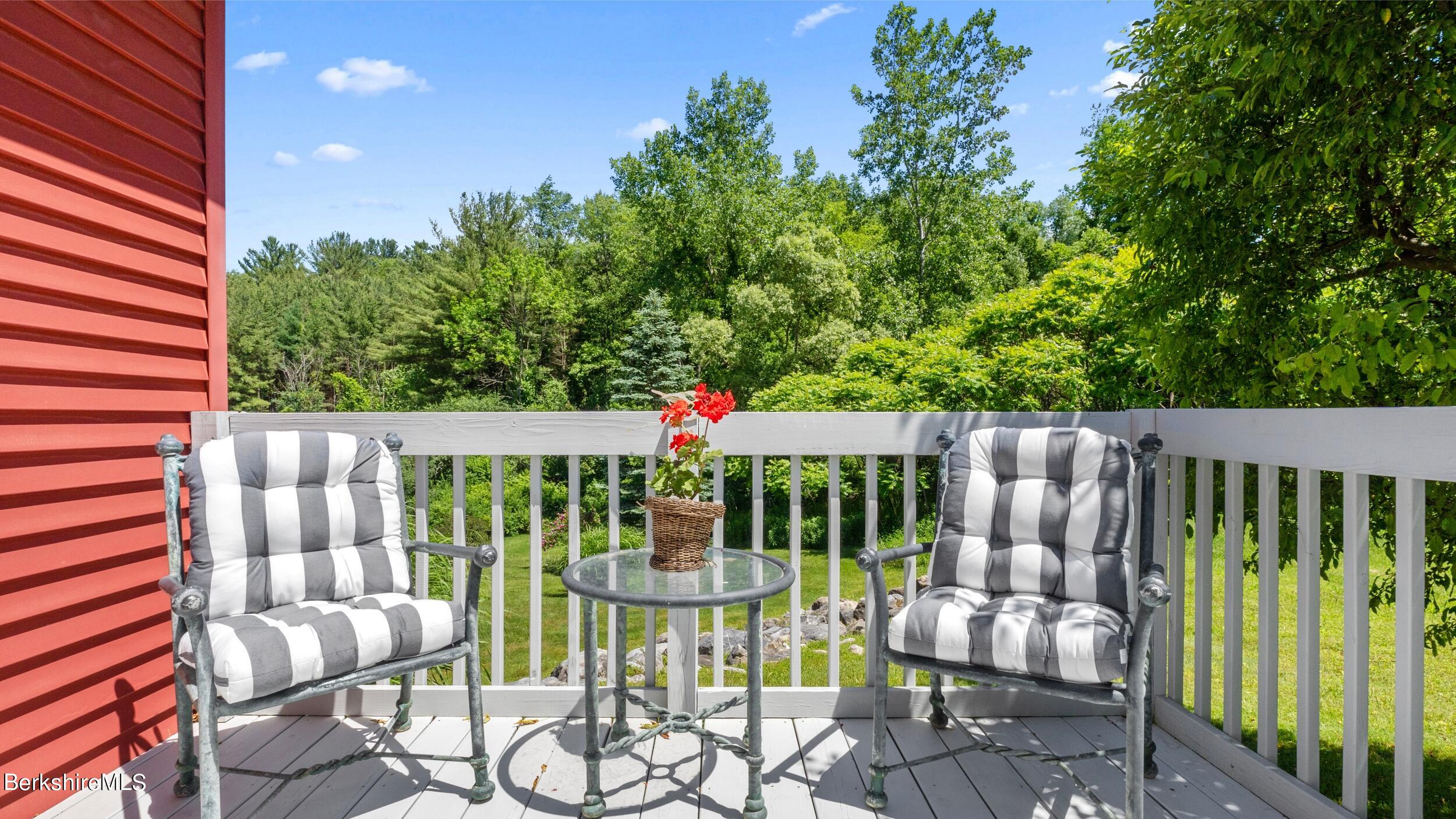 Deck with cushioned chairs and a glass table overlooking a leafy wooded yard.