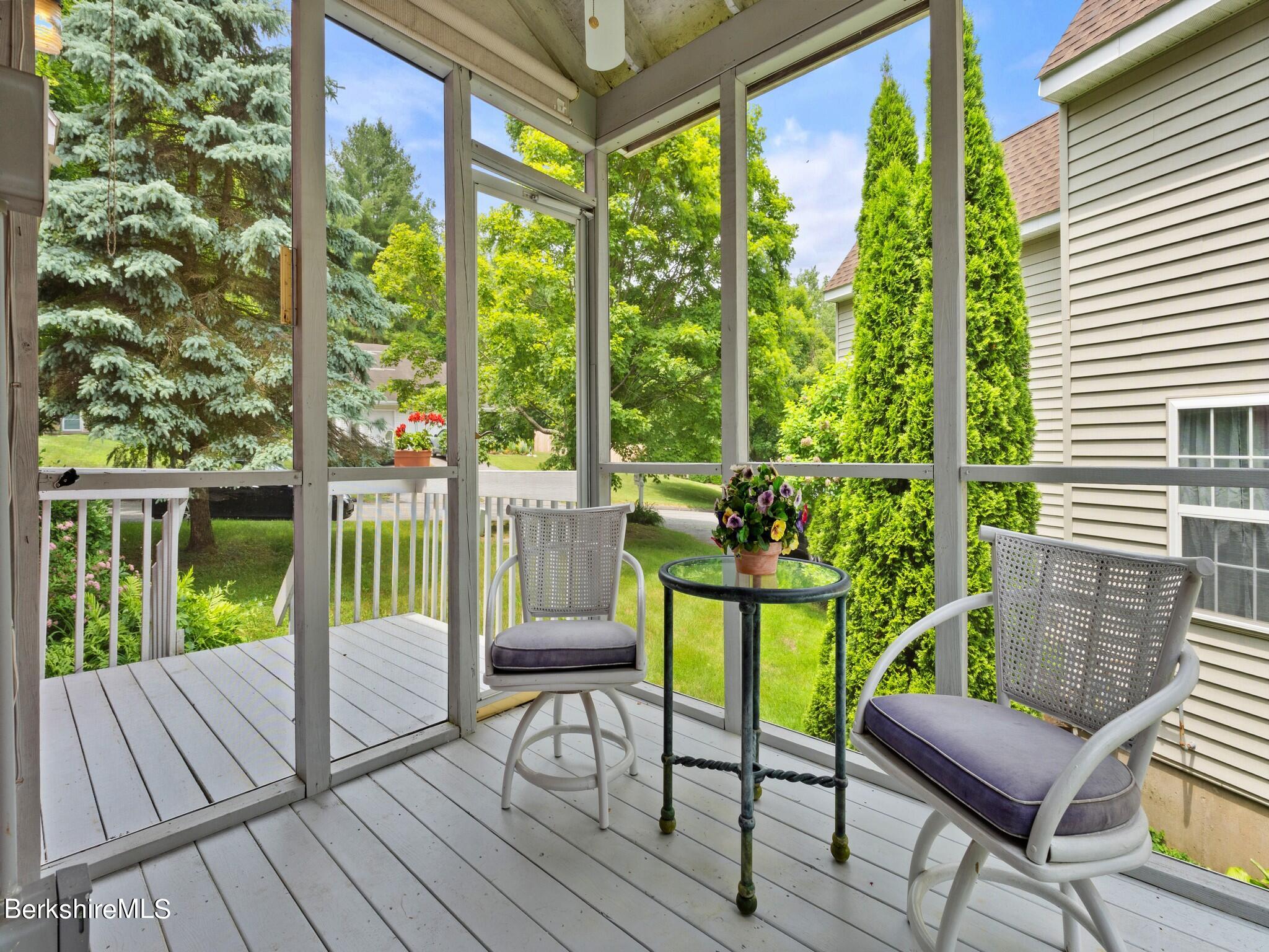 Screened porch with two cushioned chairs and a glass table overlooking a leafy yard.