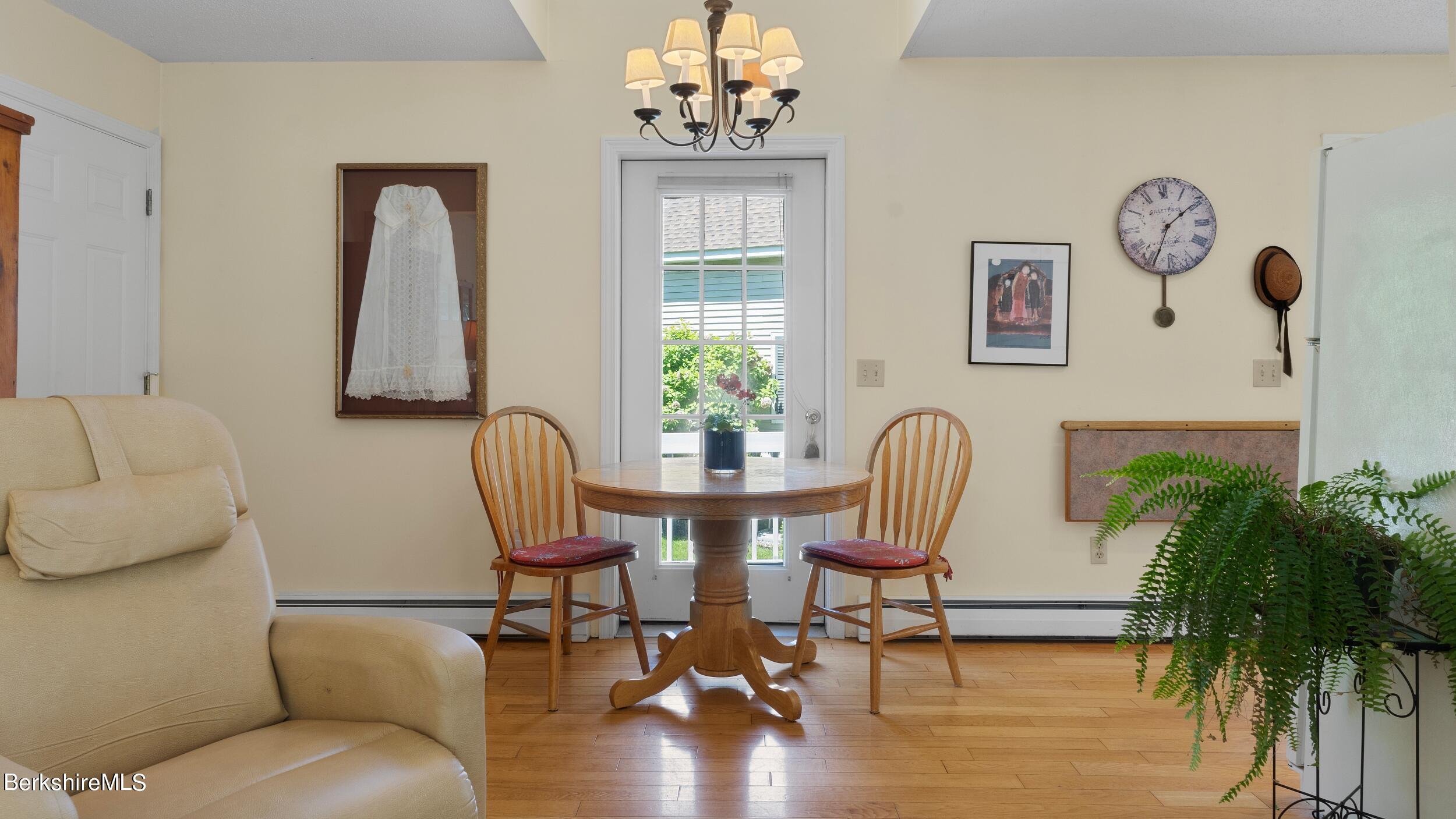 Dining area with a round wooden table, two chairs, glass-paneled door, and large fern.