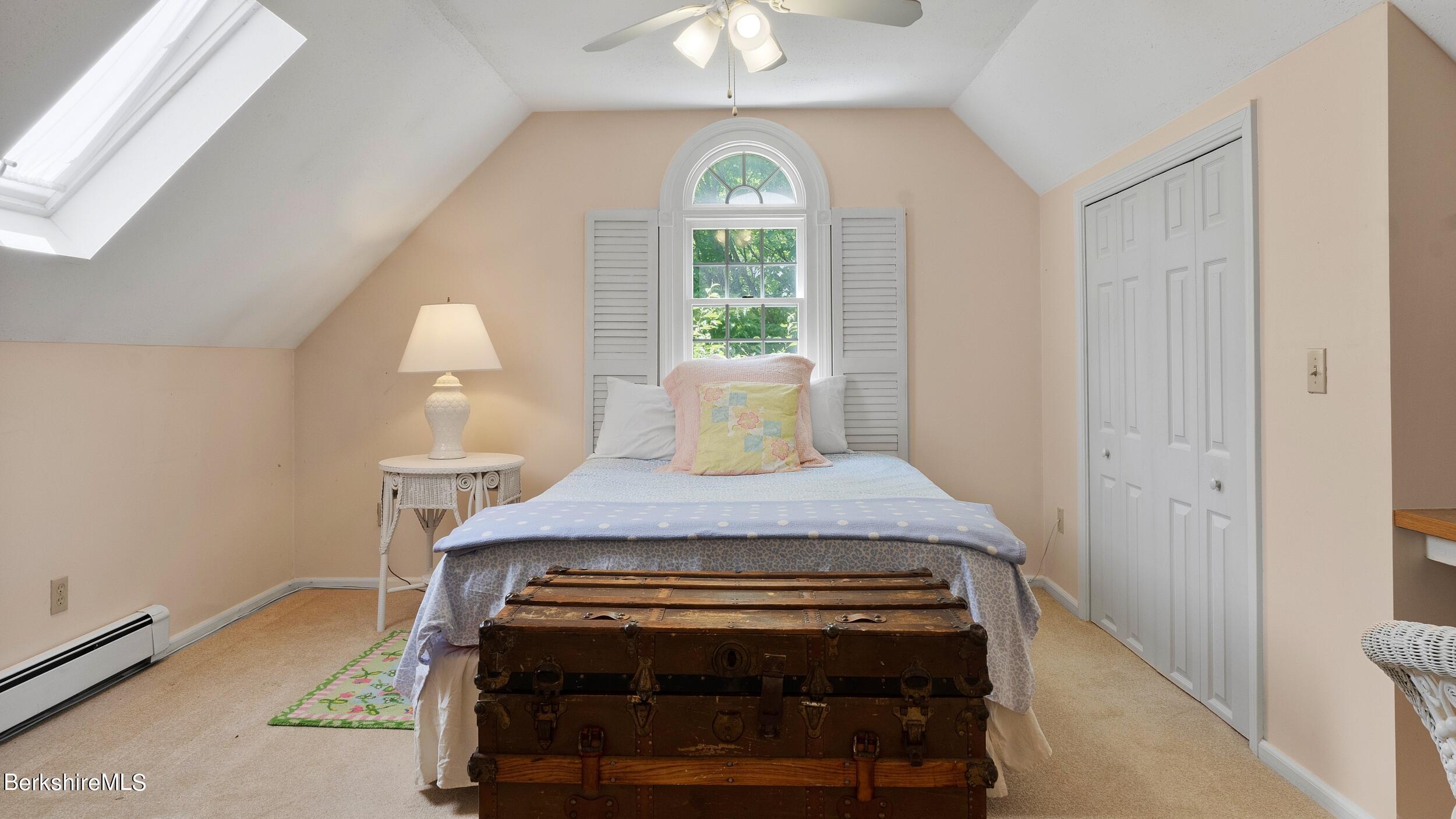 Attic bedroom with a bed beneath an arched shuttered window and an antique trunk at its foot.