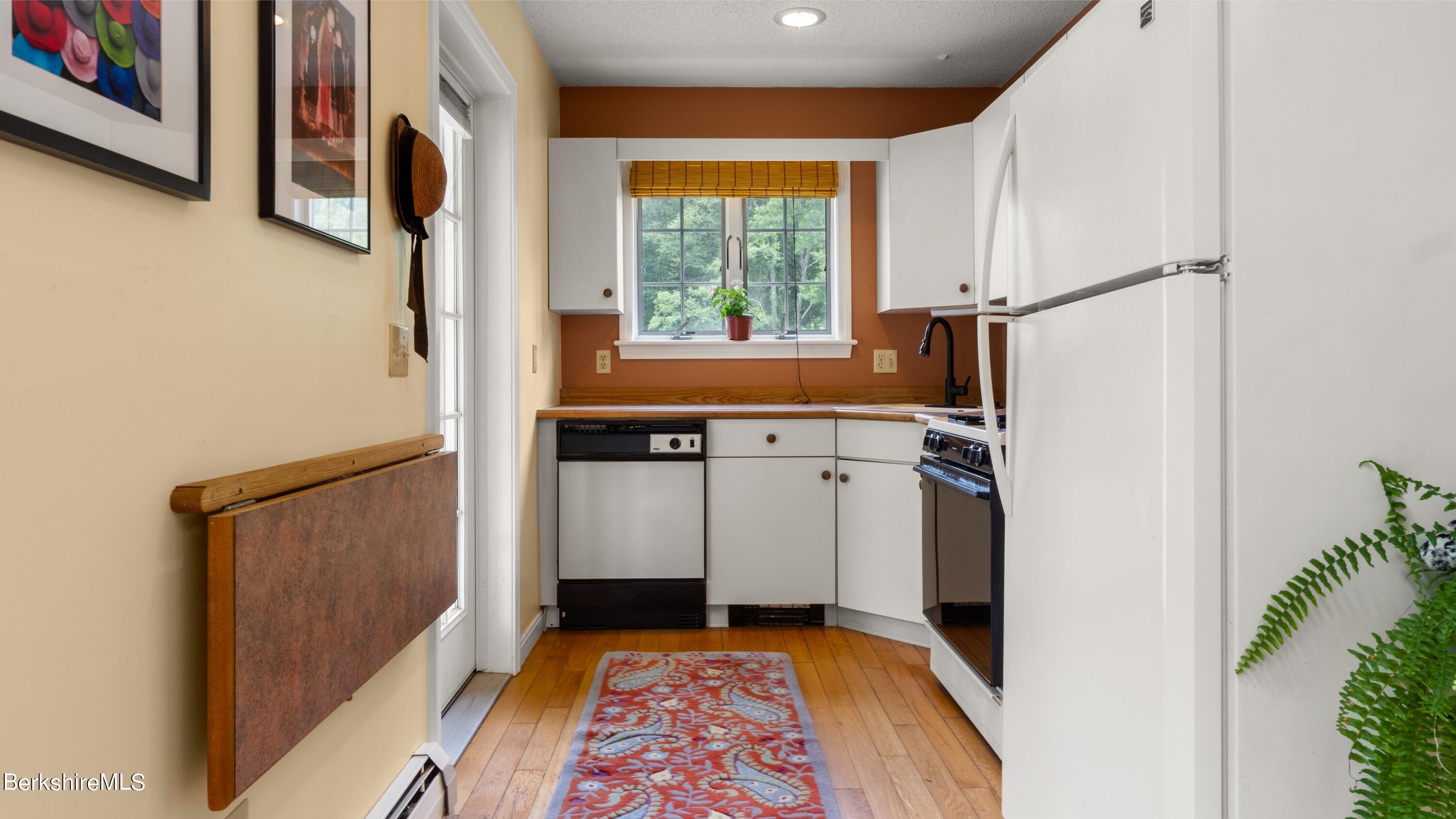 Kitchen with white cabinets, wood countertops, plank flooring, and a window overlooking trees.