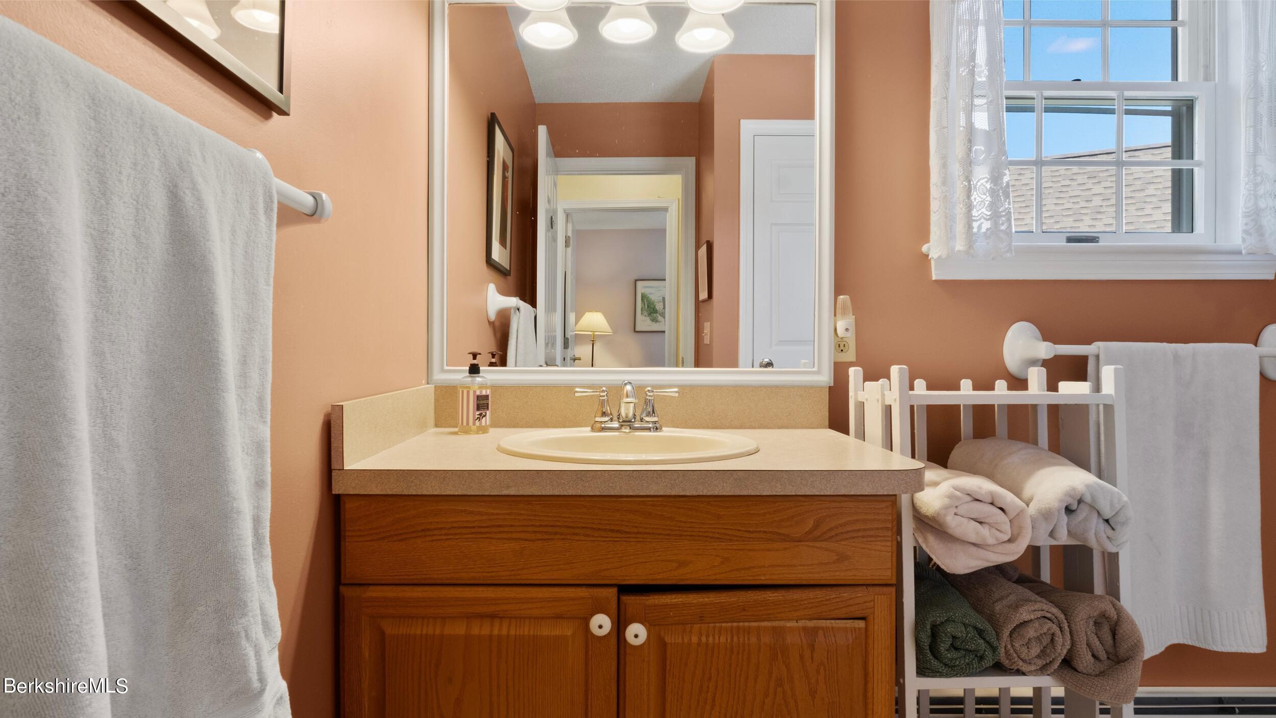 Bathroom with a wood vanity, oval sink, large mirror, and towel rack beneath a window.