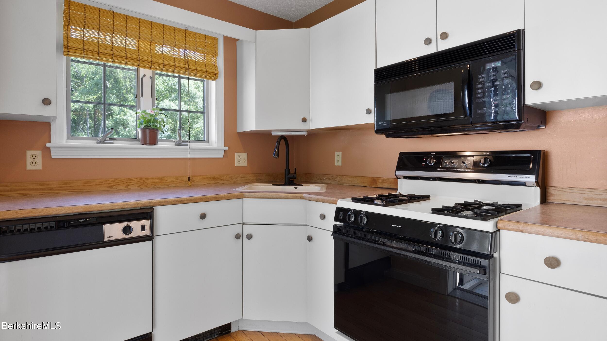 Kitchen with white cabinets, wood countertops, a window-side sink, and a white gas range.