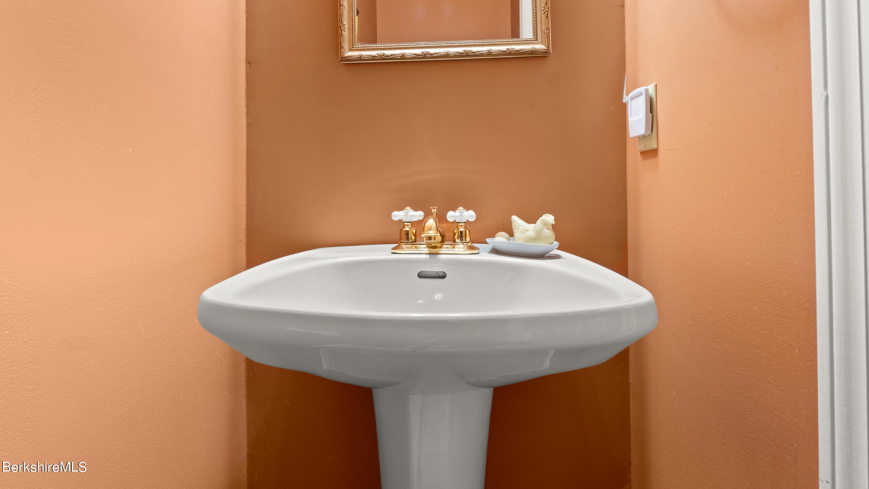 White pedestal sink with gold fixtures against terracotta-orange bathroom walls.