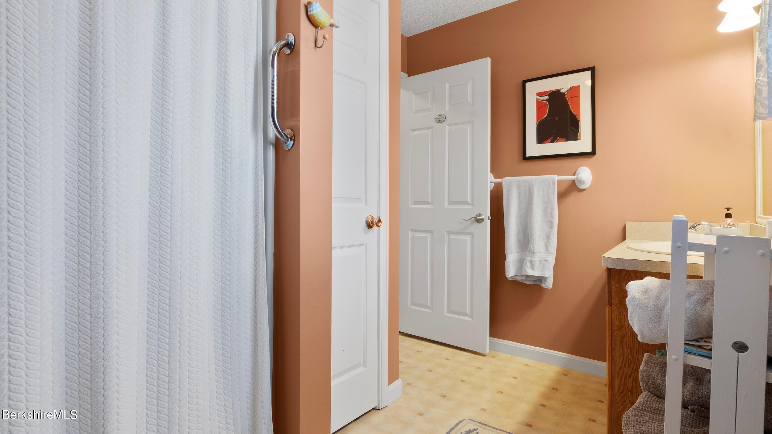 Bathroom with peach walls, a white shower curtain, and a wood vanity with sink.