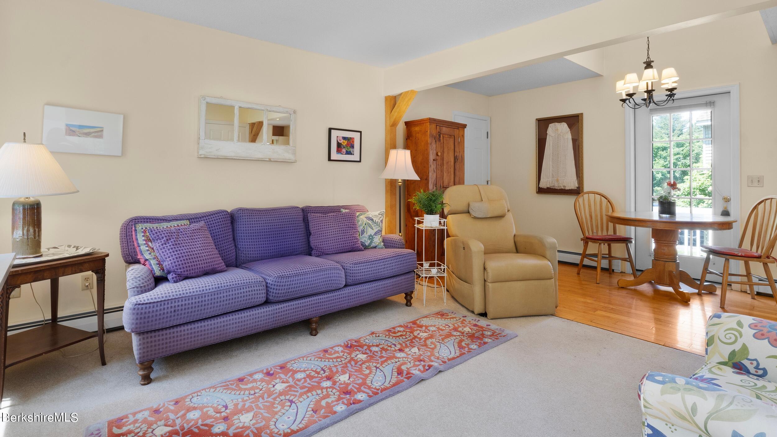 Living room with a purple patterned sofa, beige recliner, and adjoining dining area by glass-paned doors.
