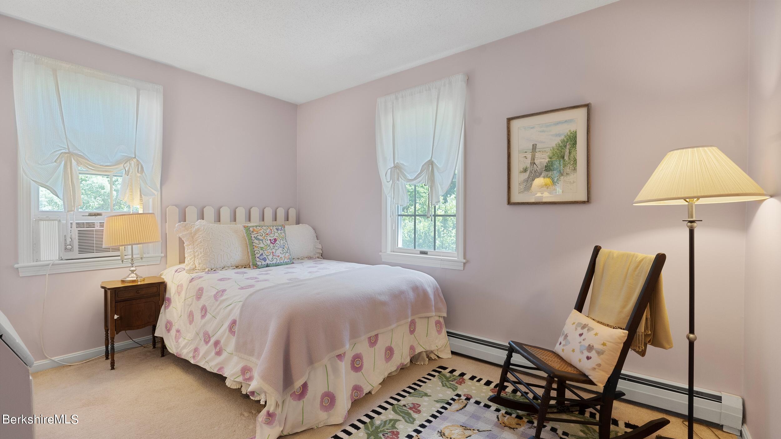 Furnished bedroom with floral bedding, pale pink walls, and a wooden chair beside the bed.