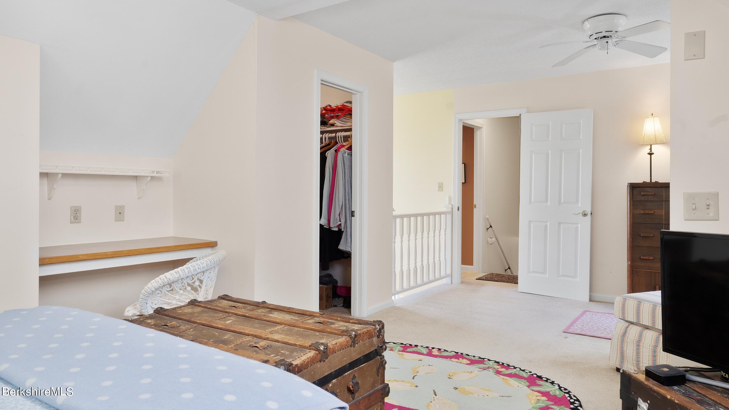 Bedroom with an open closet, ceiling fan, and antique wooden trunk at the foot of the bed.