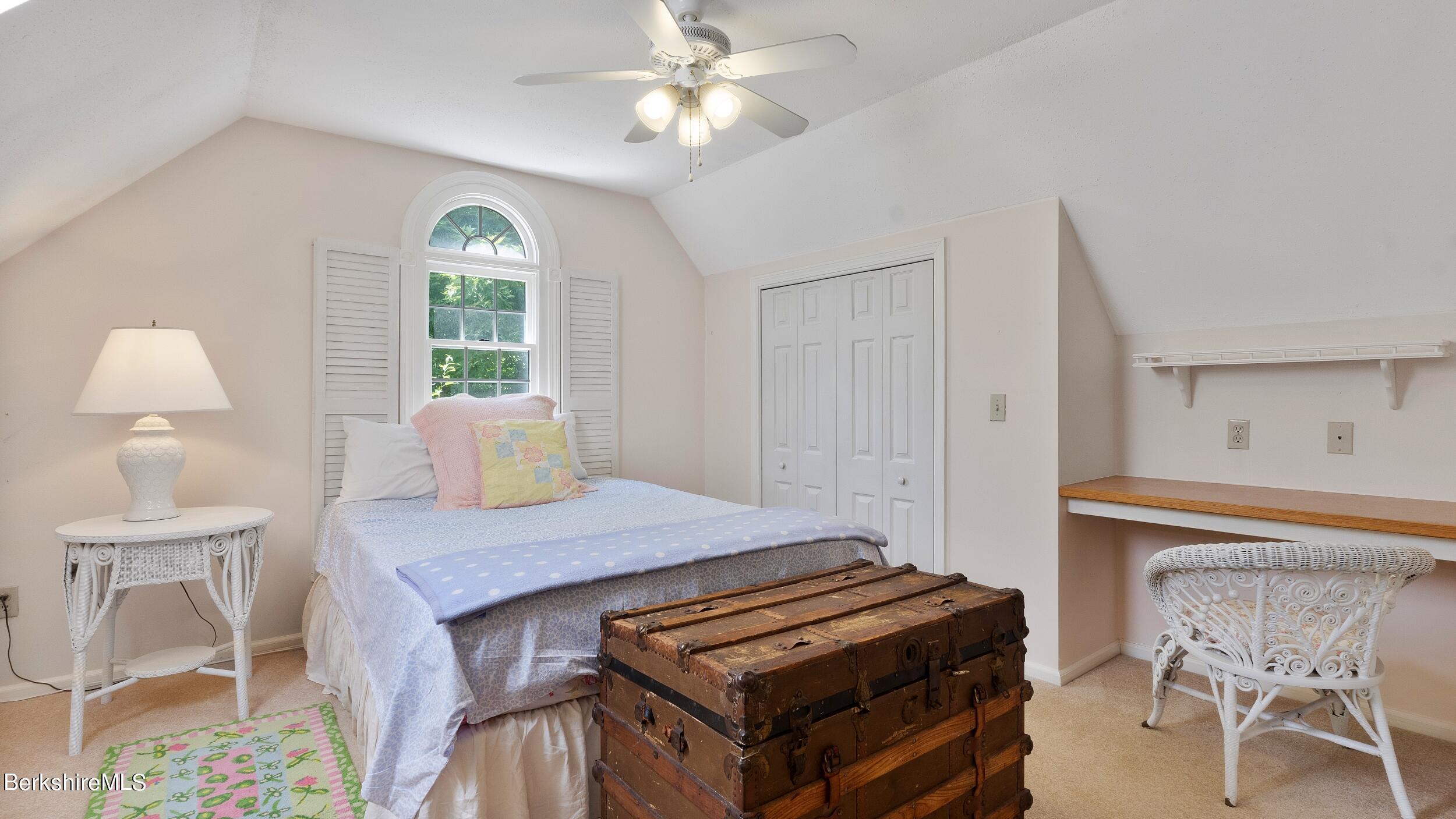 Bedroom with an arched shuttered window, a wooden trunk, and a built-in desk.