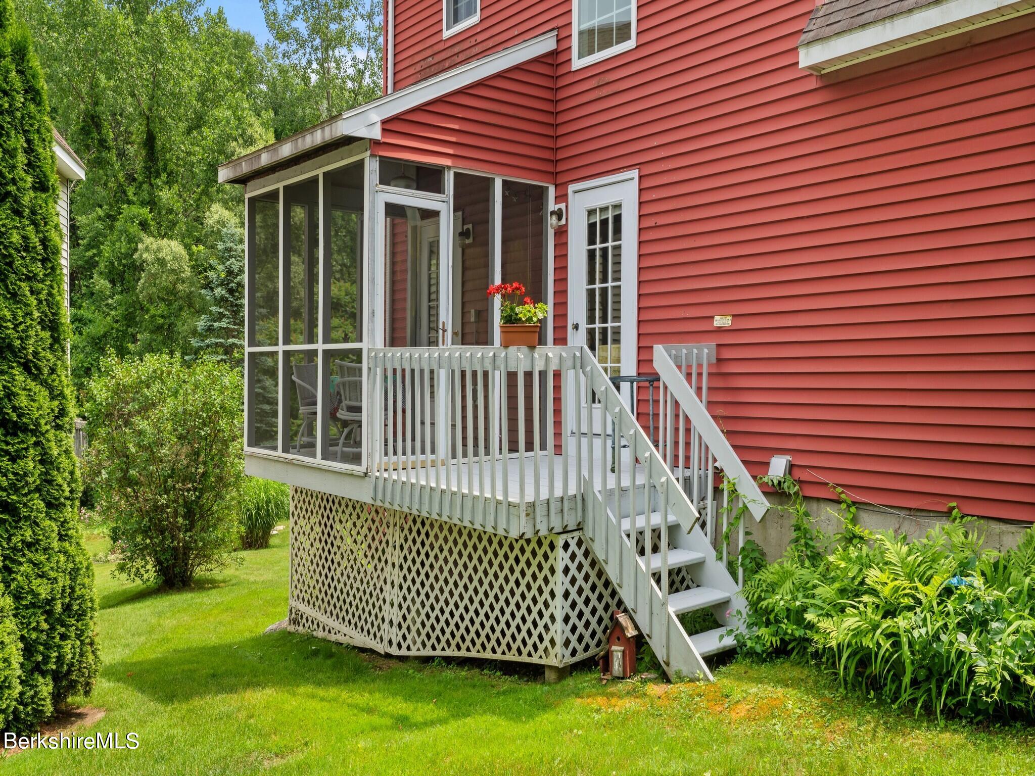 Red-sided home with a white-railed deck, screened porch, and landscaped yard.