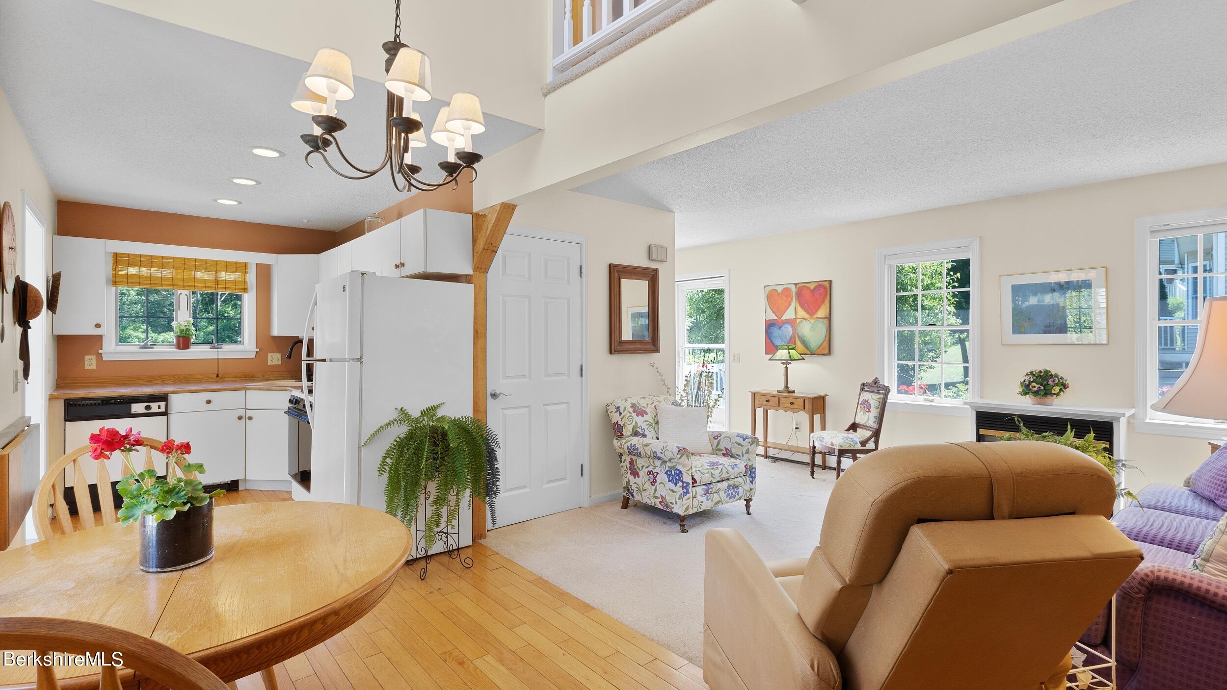 Open-plan living room and kitchen with white cabinets, wood dining table, and floral armchairs.