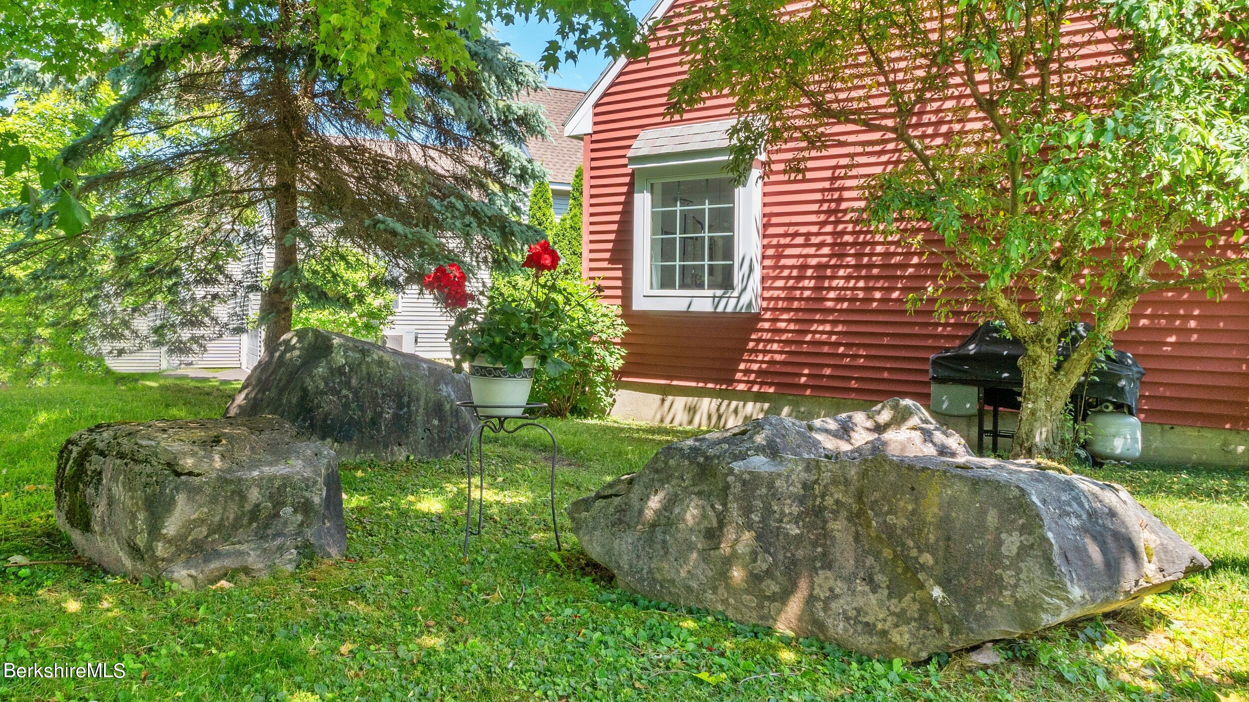 Red-sided home beside a leafy yard with large boulders and a potted flowering plant.