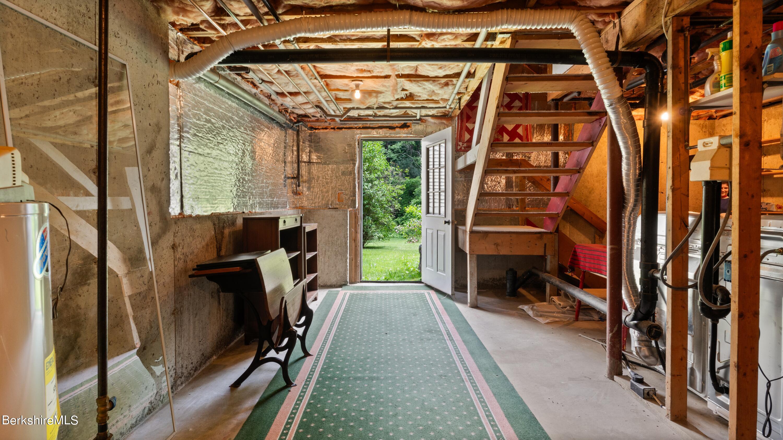 Basement with exposed framing and ductwork, stairs, and an open door to the yard.