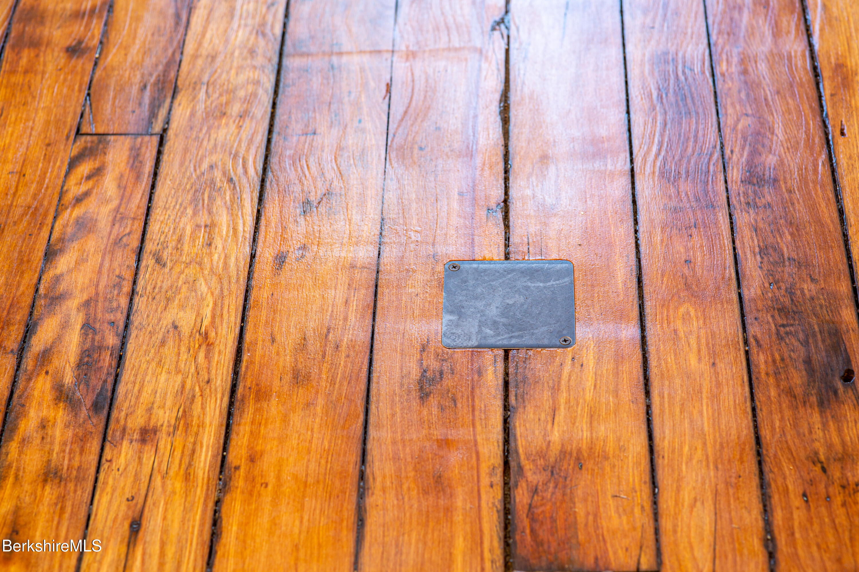 Wood floorboards with a small rectangular metal access plate.
