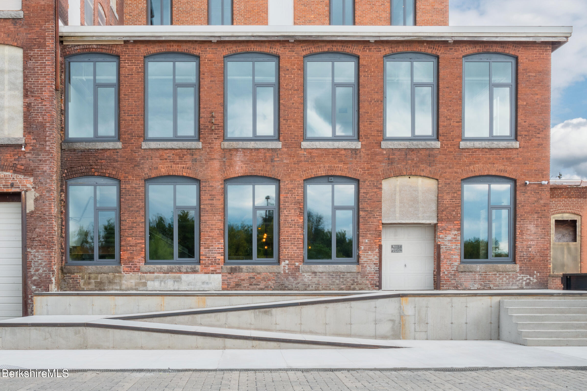 Red-brick building with tall gray-framed windows and a concrete accessibility ramp.