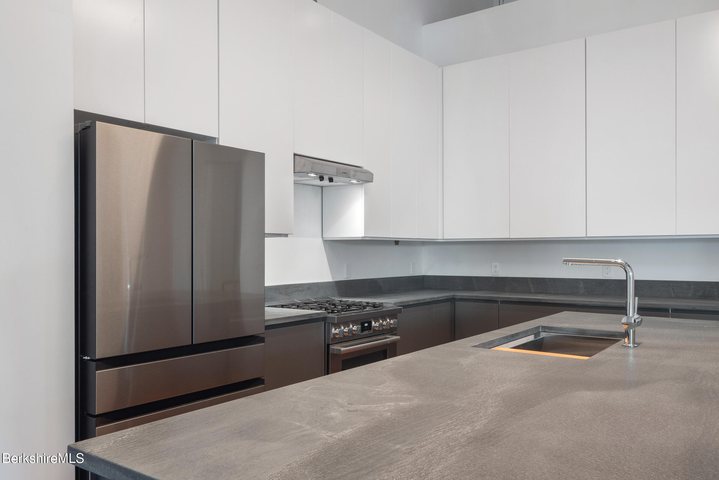Modern kitchen with a large gray stone island, undermount sink, and stainless steel appliances.