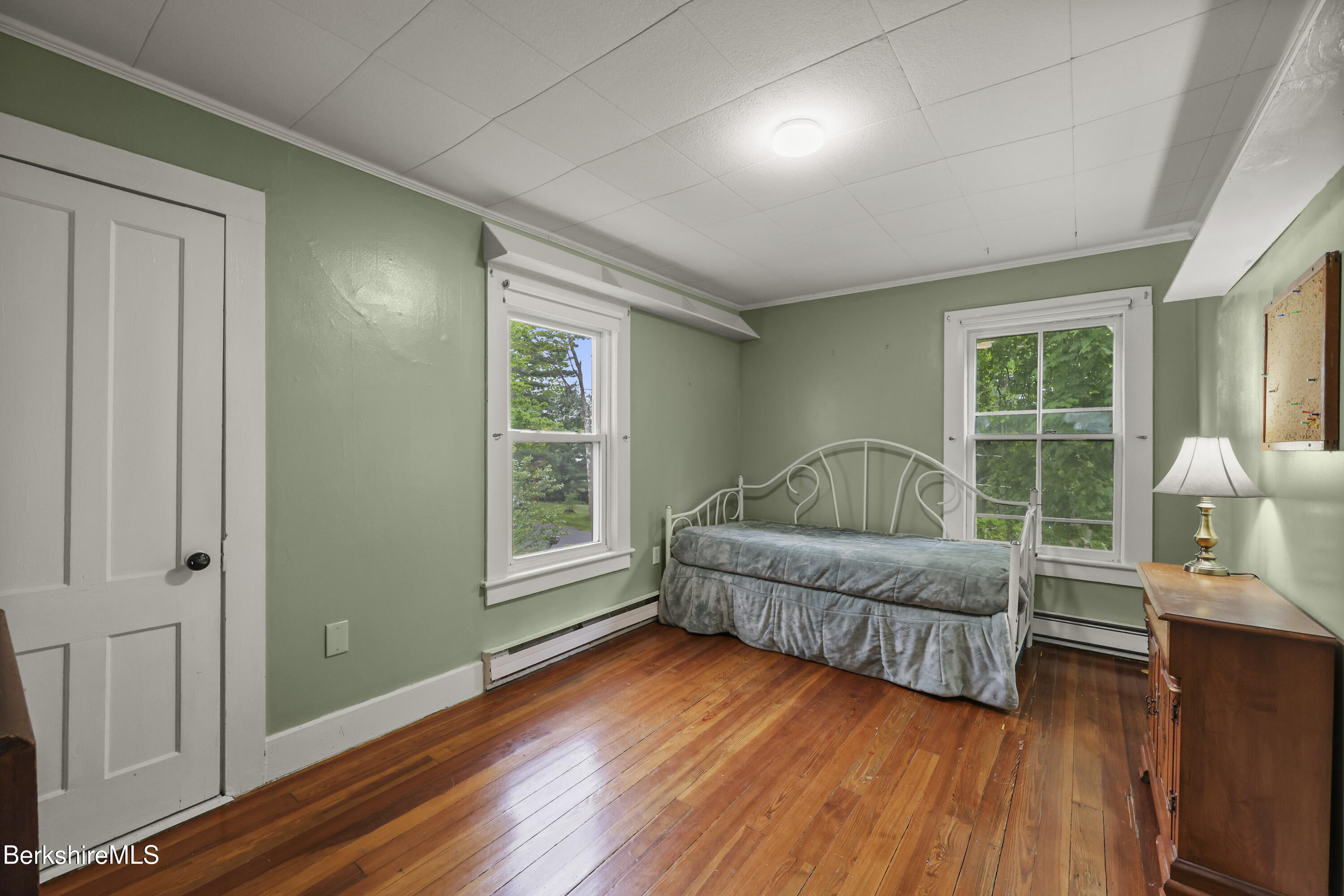 Bedroom with a white metal daybed, sage-green walls, two windows, and polished hardwood floors.