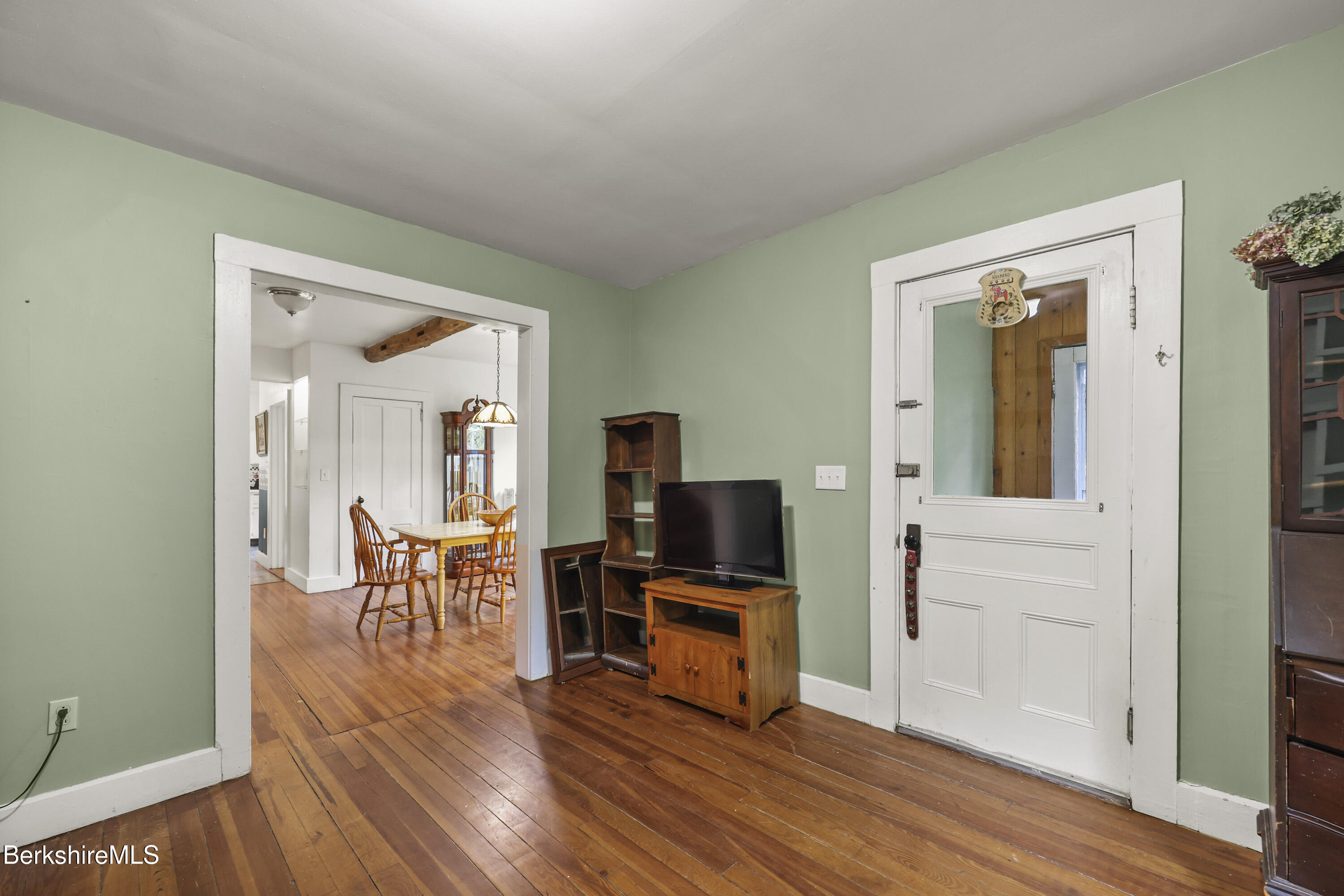 Living room with green walls and wood floors, opening to a dining area with a wooden table.