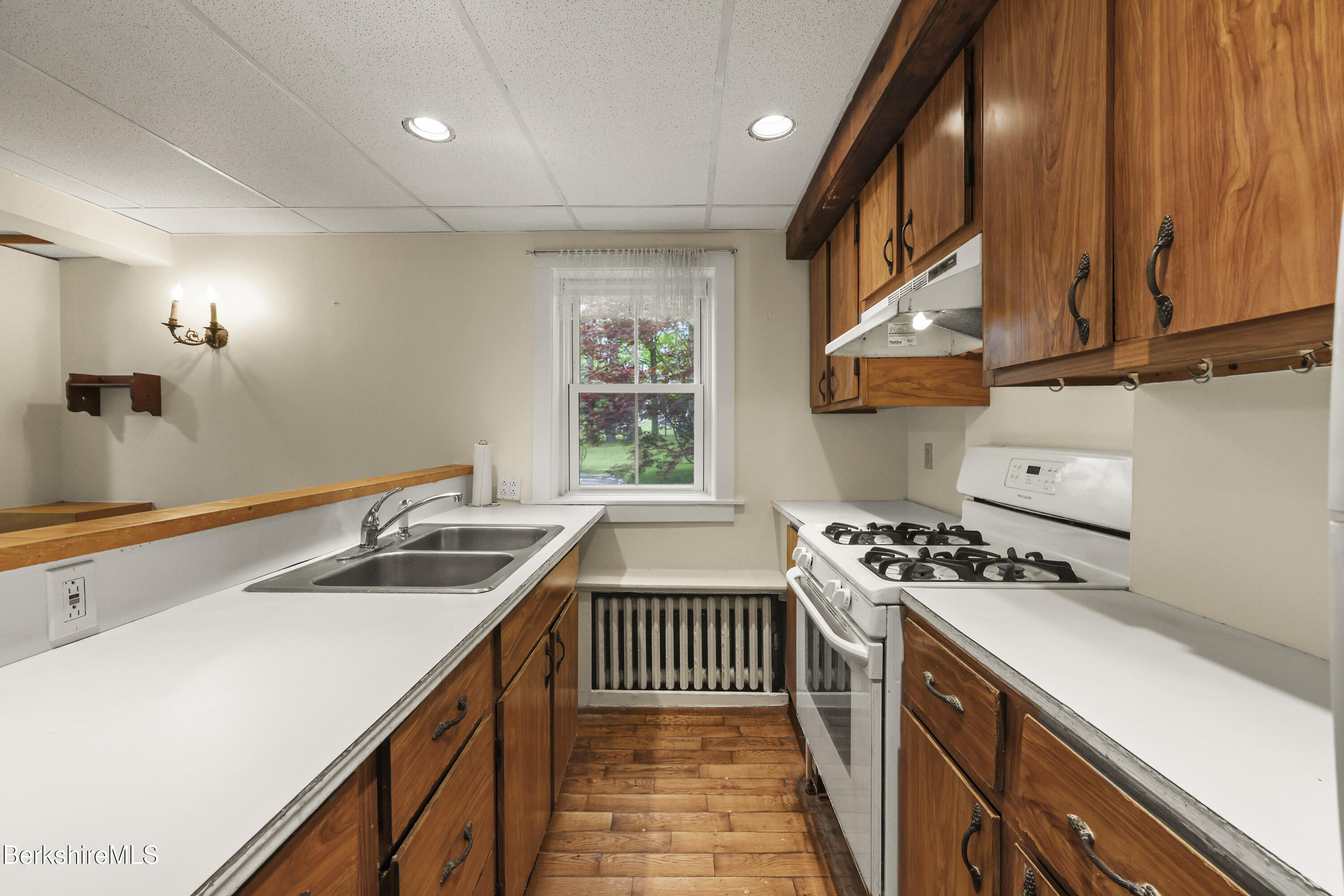 Kitchen with warm wood cabinets, a white gas range, double sink, and wood plank floor.