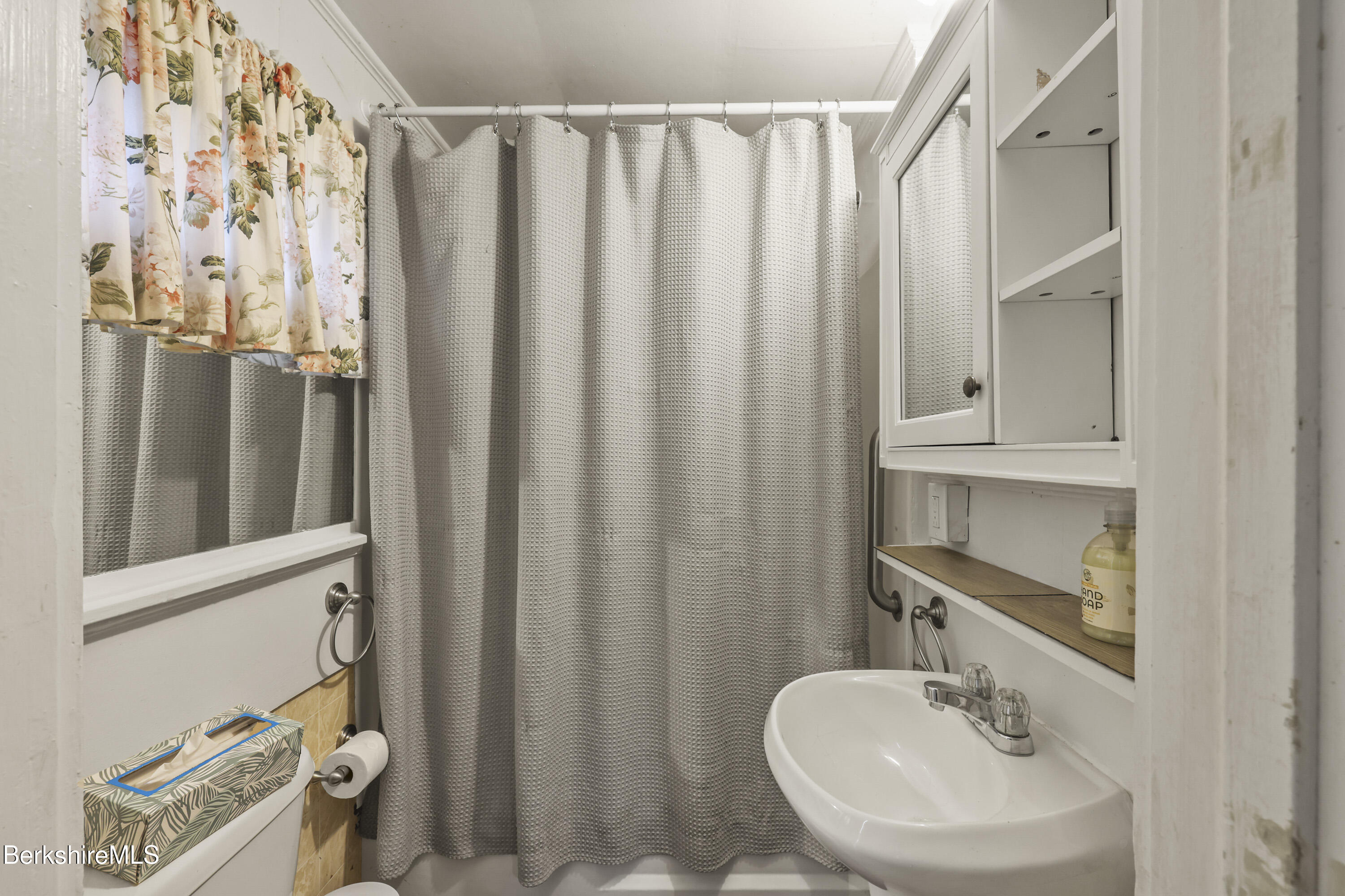Bathroom with a gray shower curtain, floral valance, mirrored cabinet, and white sink.