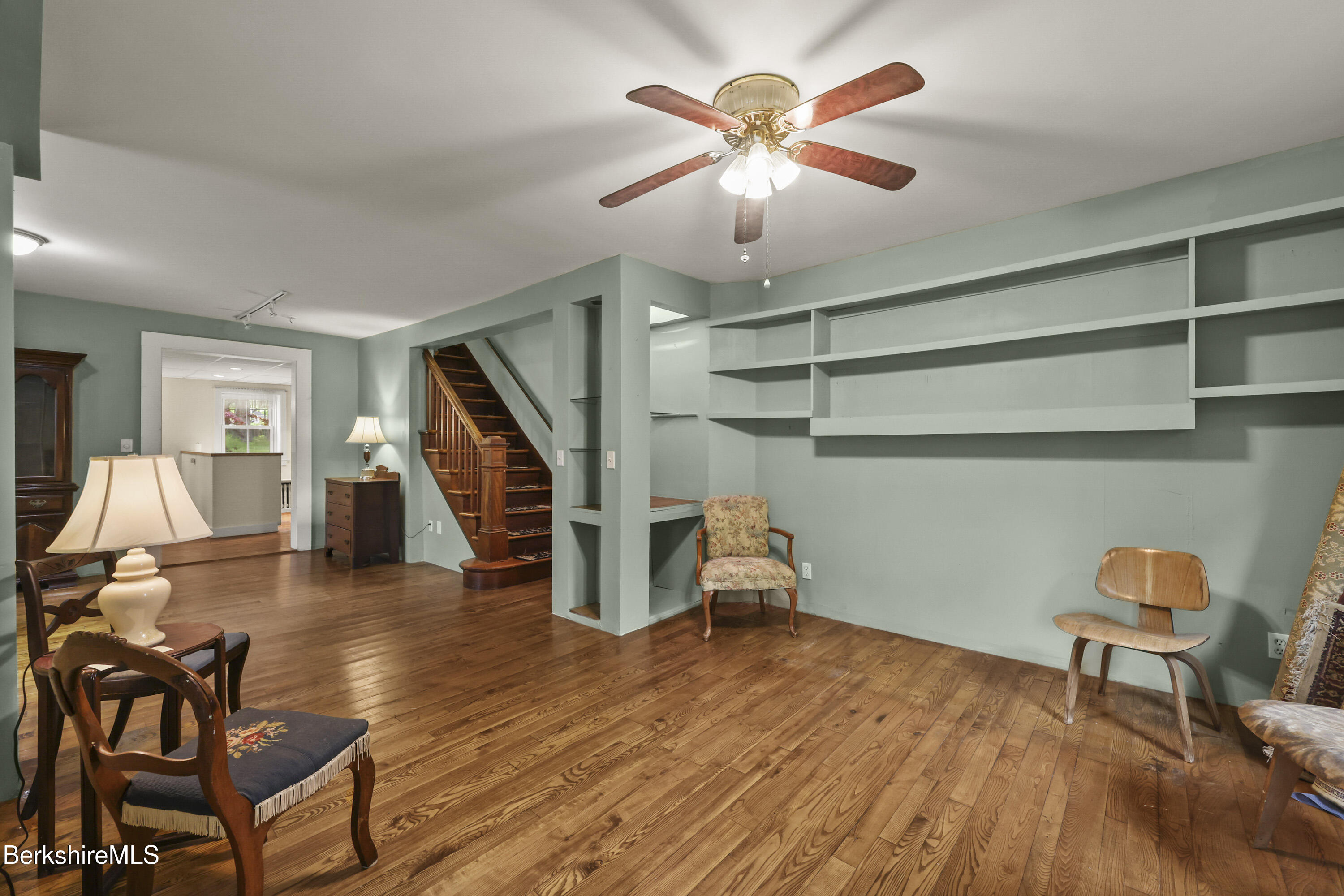 Living room with built-in shelving, a wooden staircase, and wide-plank floors.
