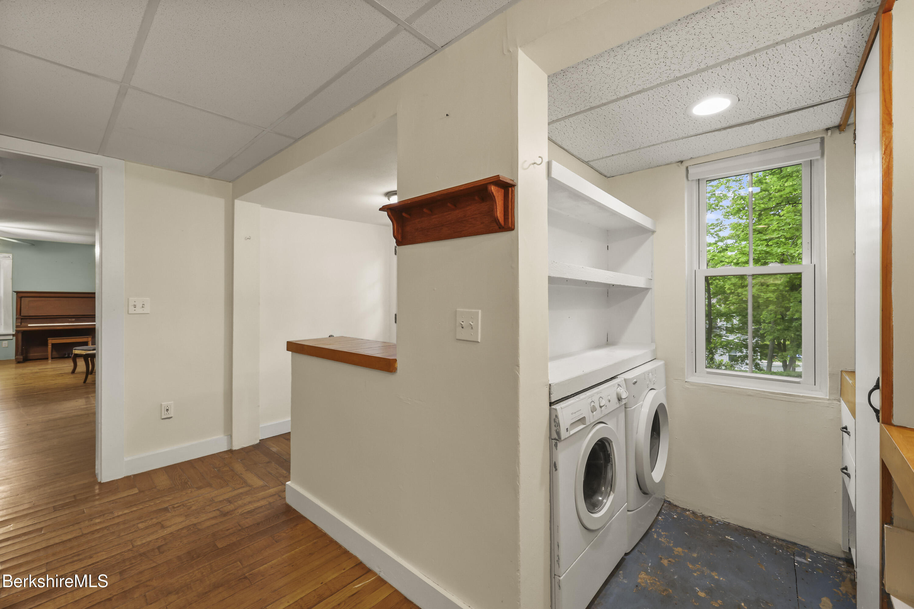 Laundry area with front-loading washer and dryer, built-in shelves, and a window overlooking trees.