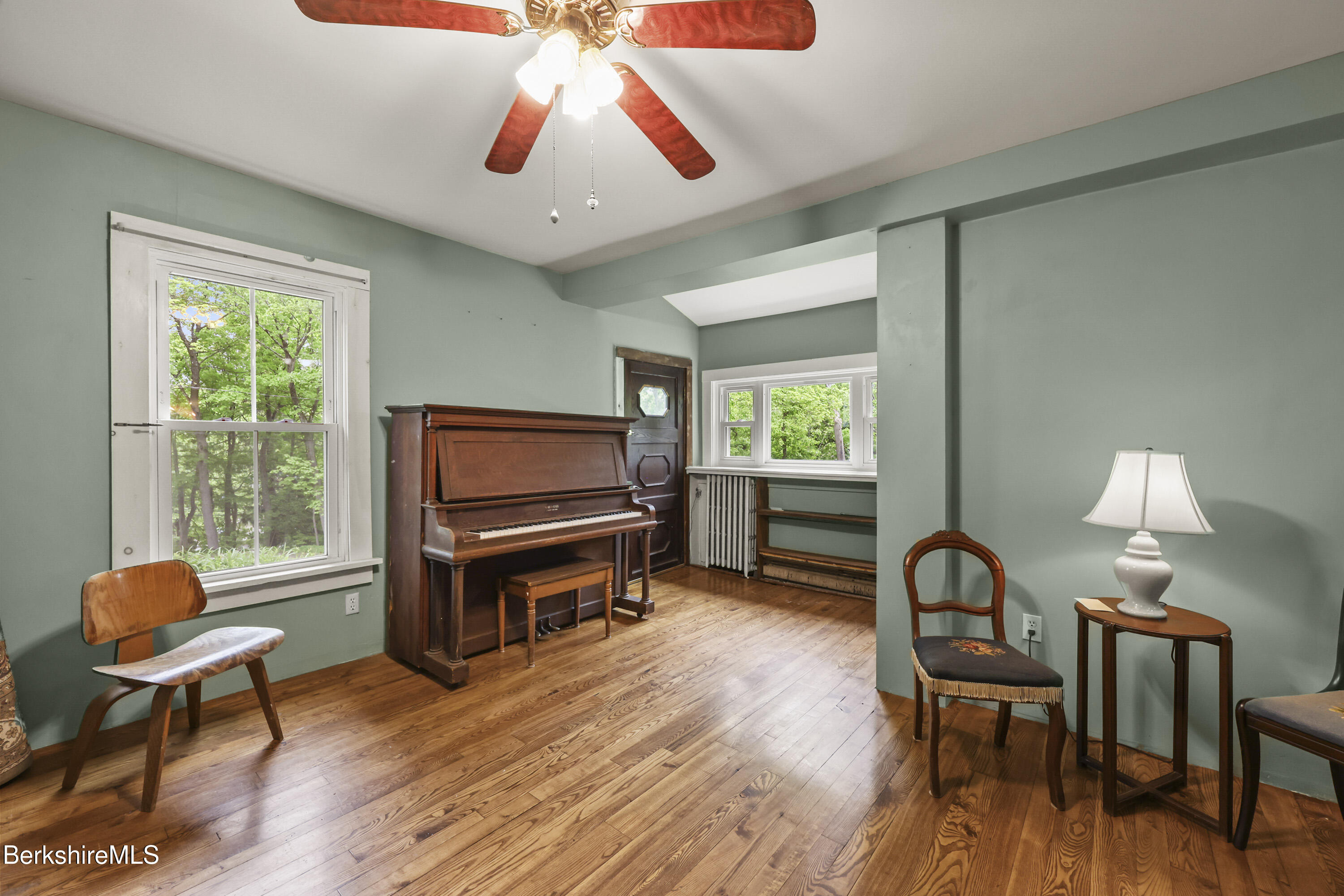 Music room with an upright piano, sage-green walls, and wide-plank hardwood floors.