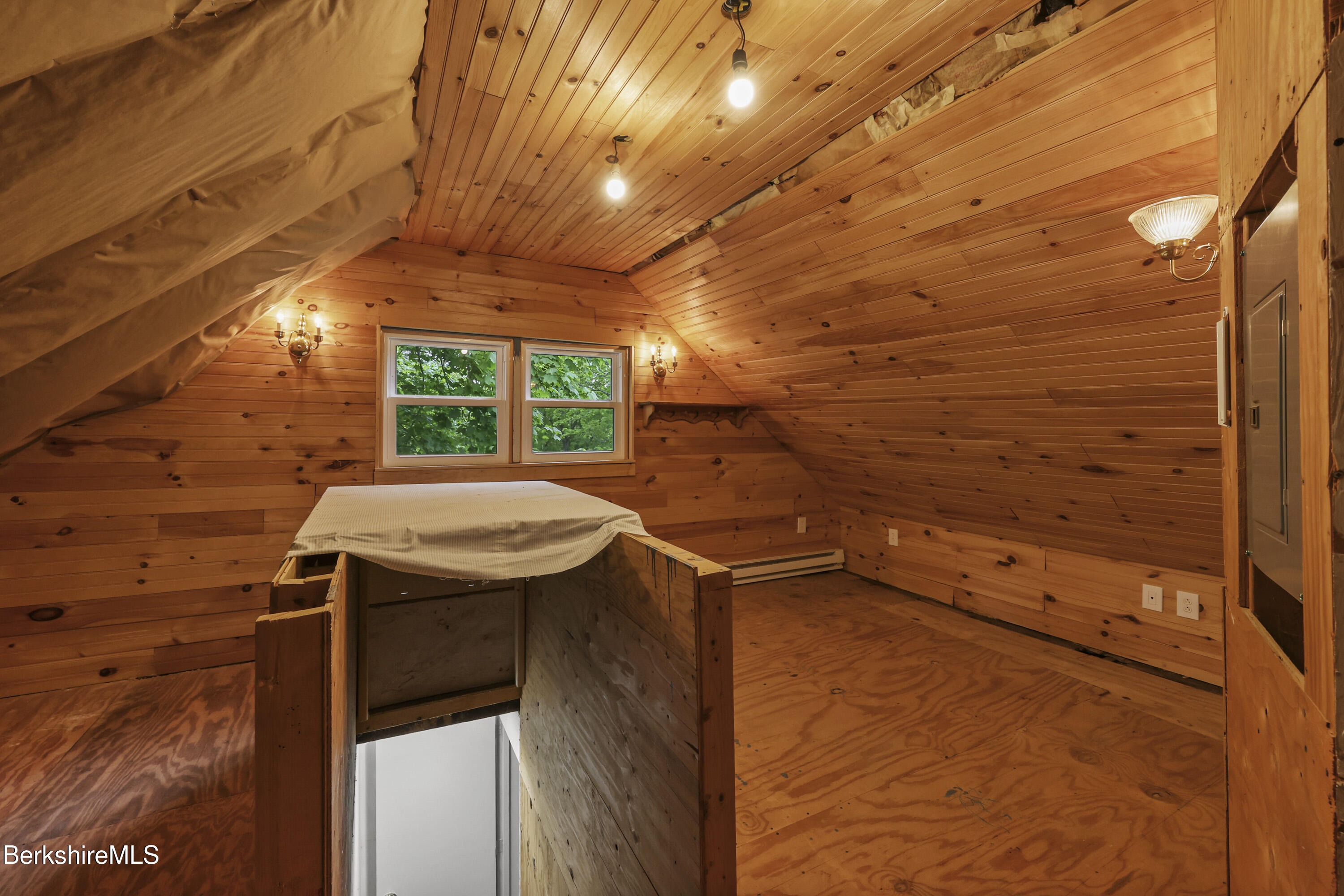 Unfinished wood-paneled attic with sloped ceiling, two windows, and an open stairwell.