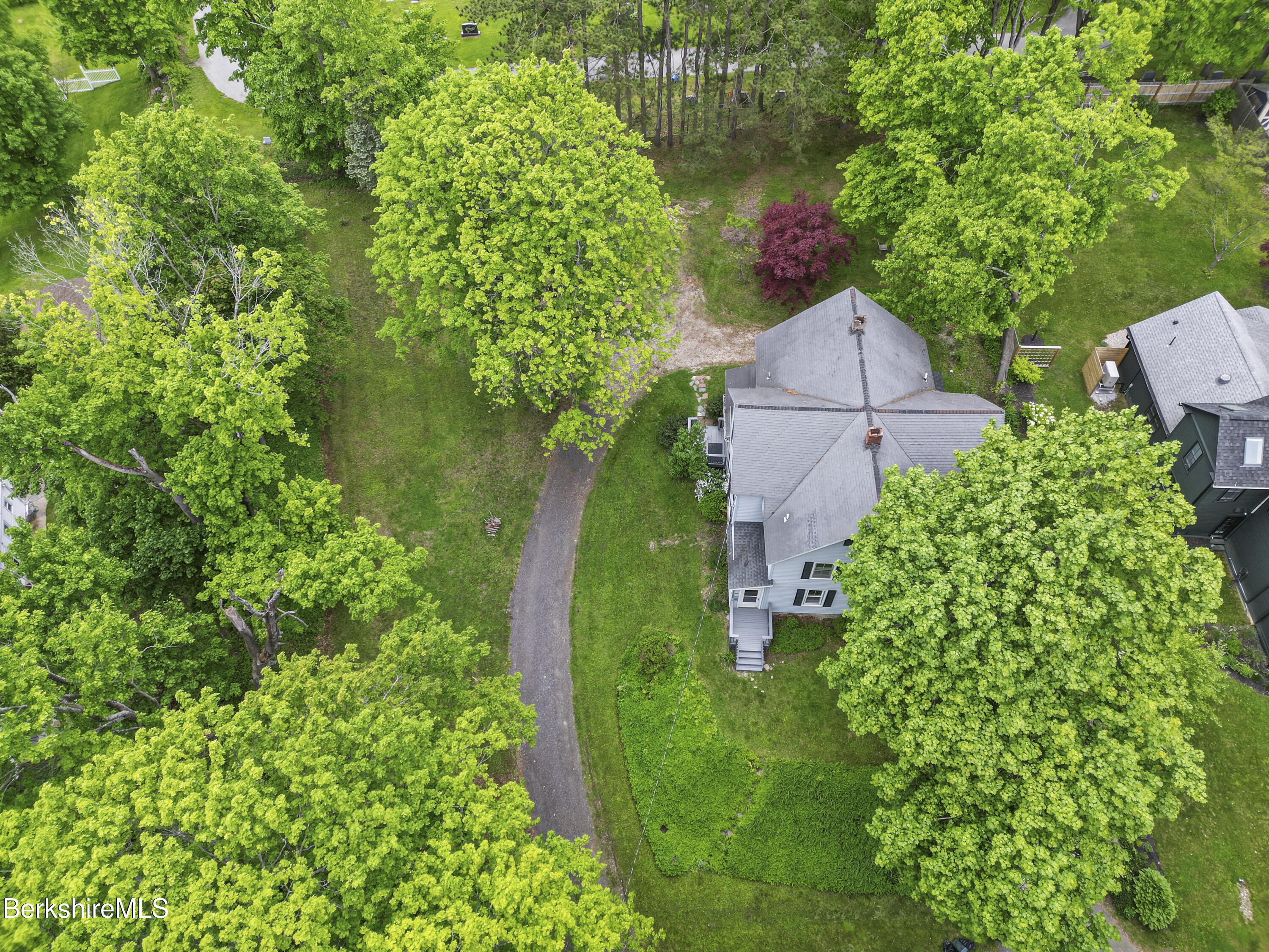 Aerial view of a gray-roofed house amid mature trees, a spacious lawn, and a curving gravel driveway.