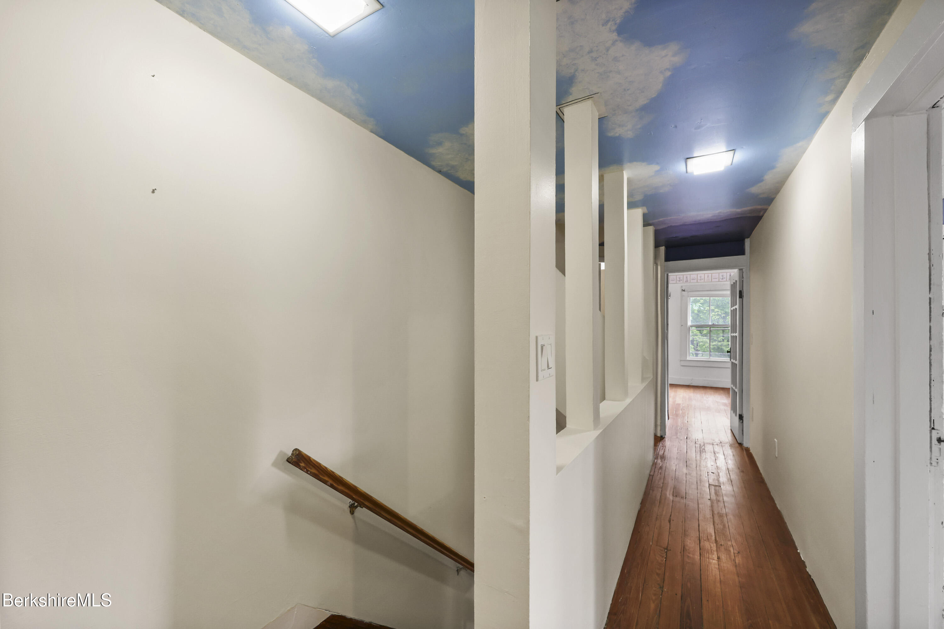 Hallway with a blue cloud-painted ceiling, wood floors, and a wooden stair handrail.