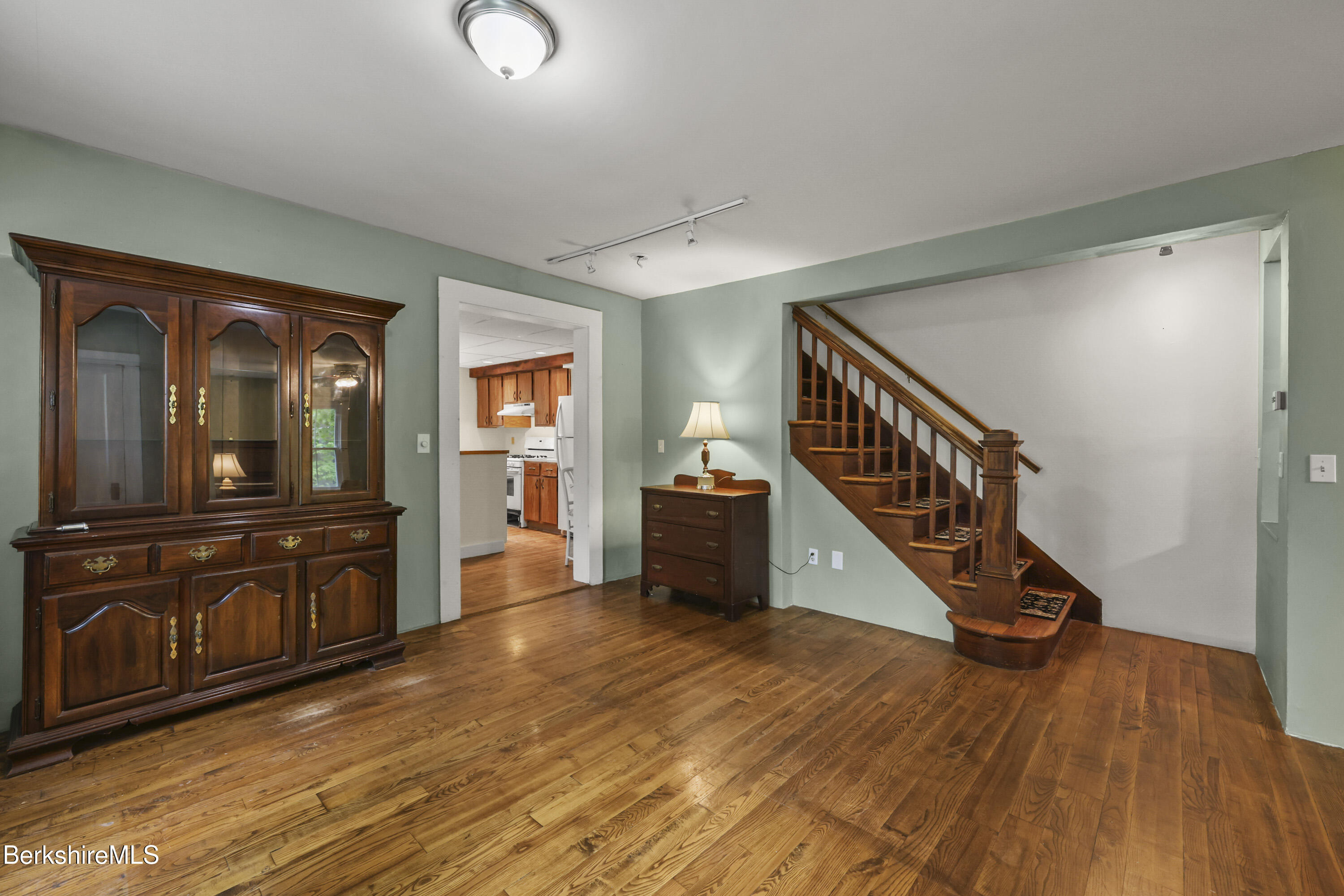 Entry hall with polished hardwood floors, a dark wood staircase, and a glass-front china cabinet.