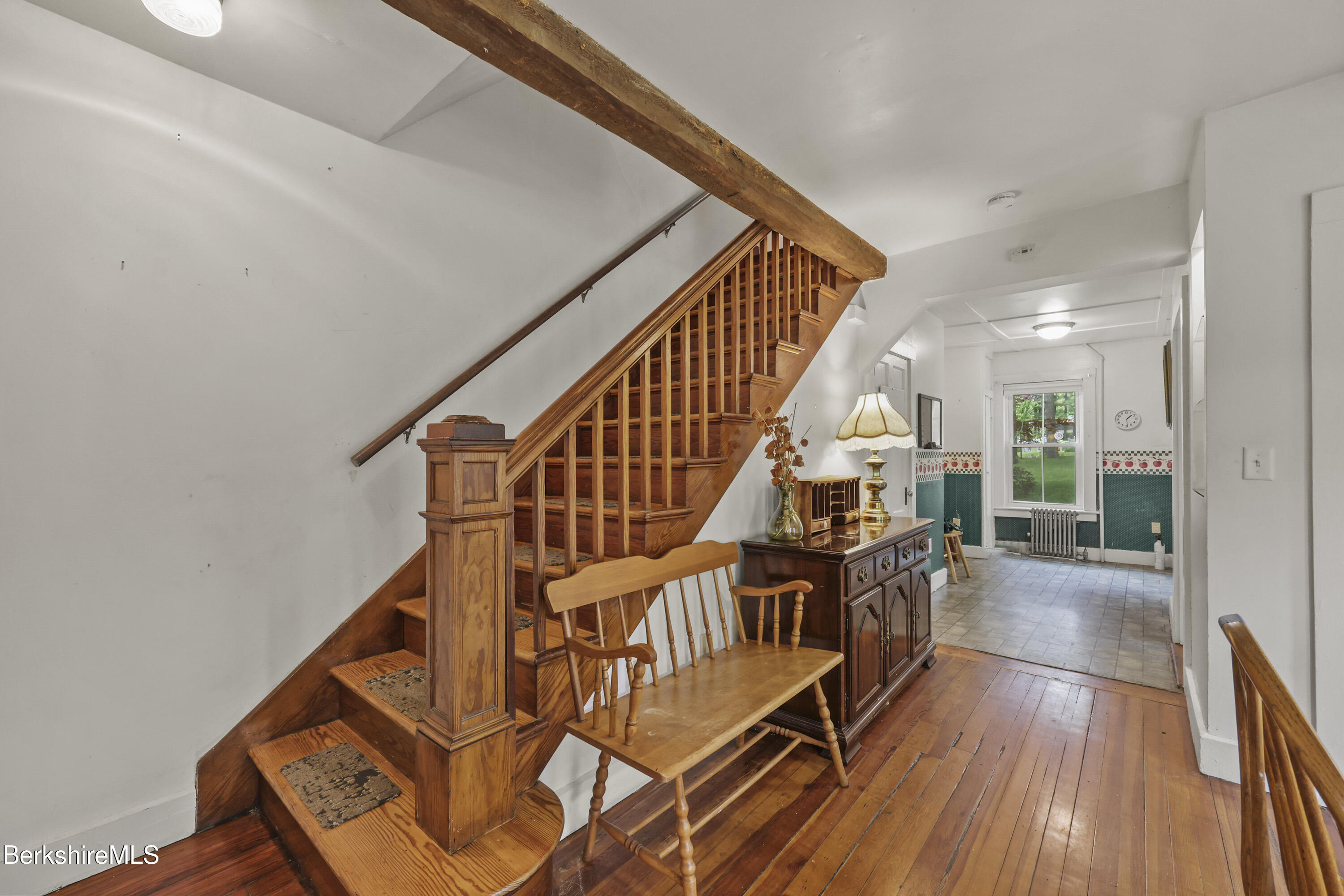 Entry hall with a wooden staircase, exposed ceiling beam, bench, and tiled room beyond.